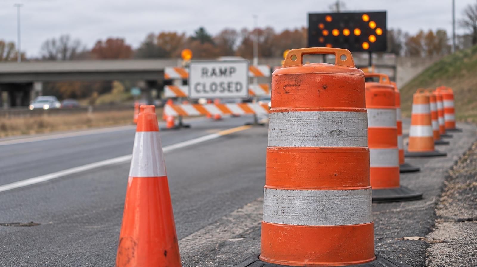 Orange traffic cones and construction barrels lining a closed highway on-ramp.