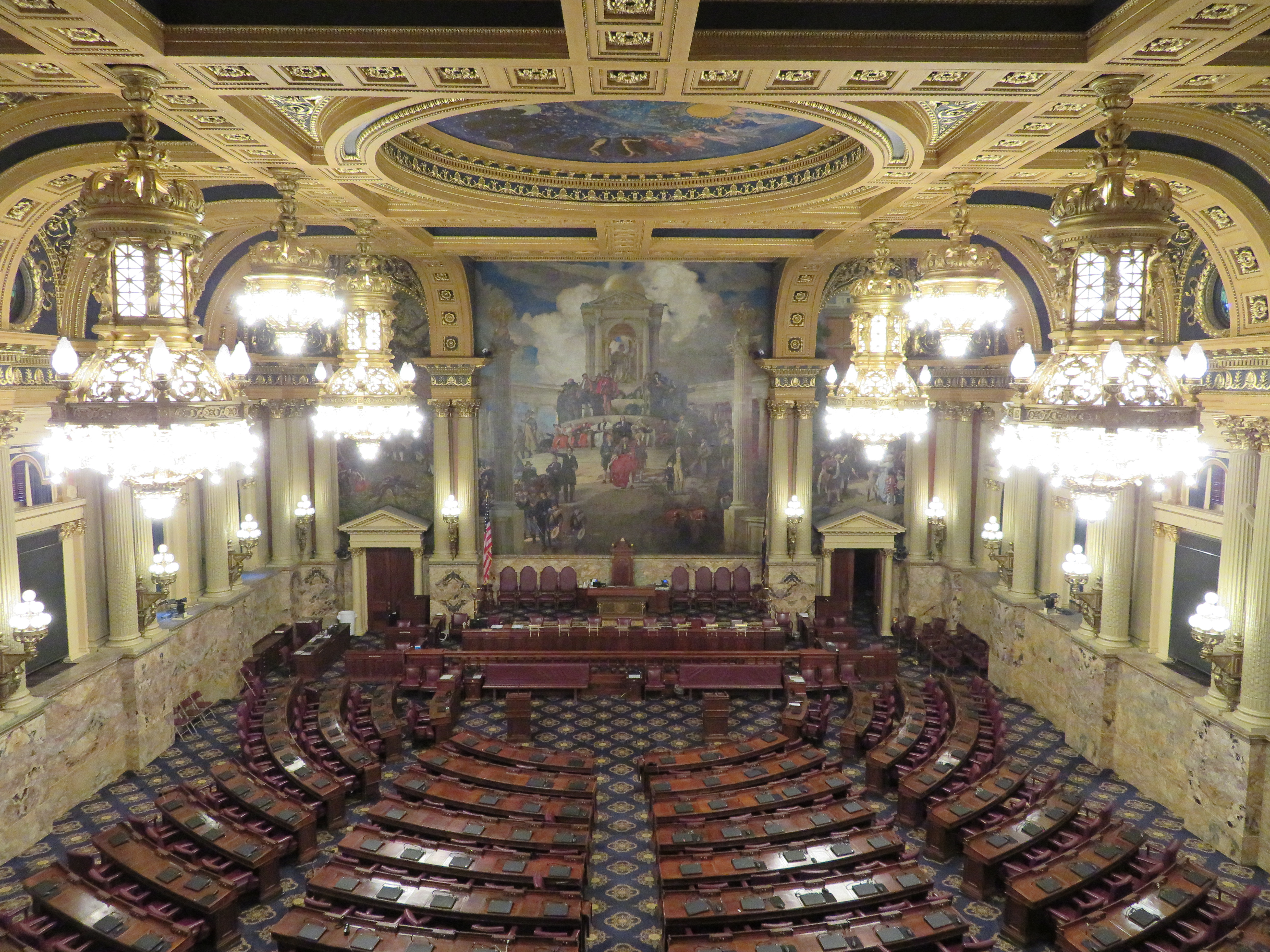 Ornate legislative chamber with semicircular rows of desks and a gilded domed ceiling.