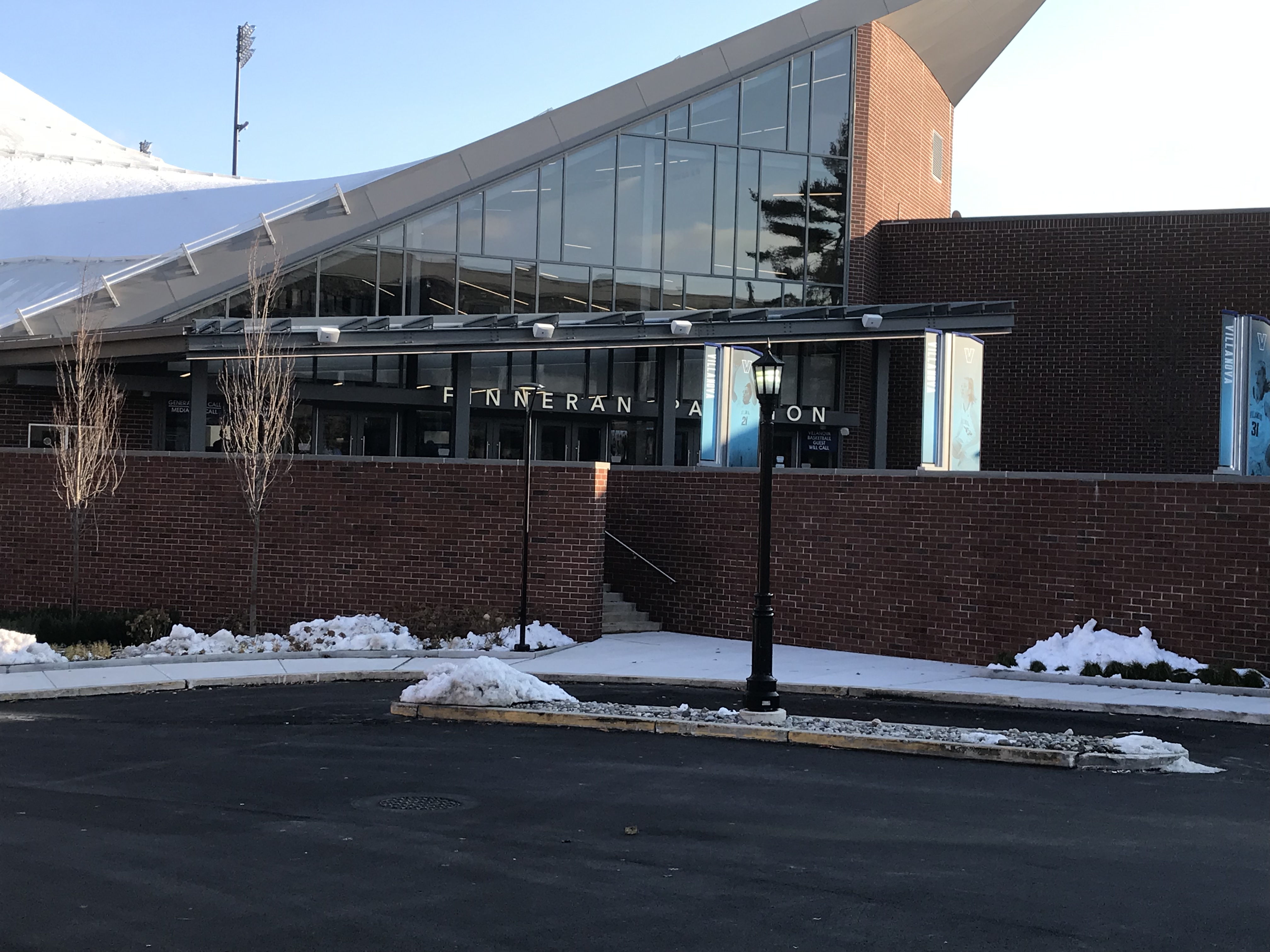 Brick and glass arena exterior with snow on the ground and a lamp post in front.