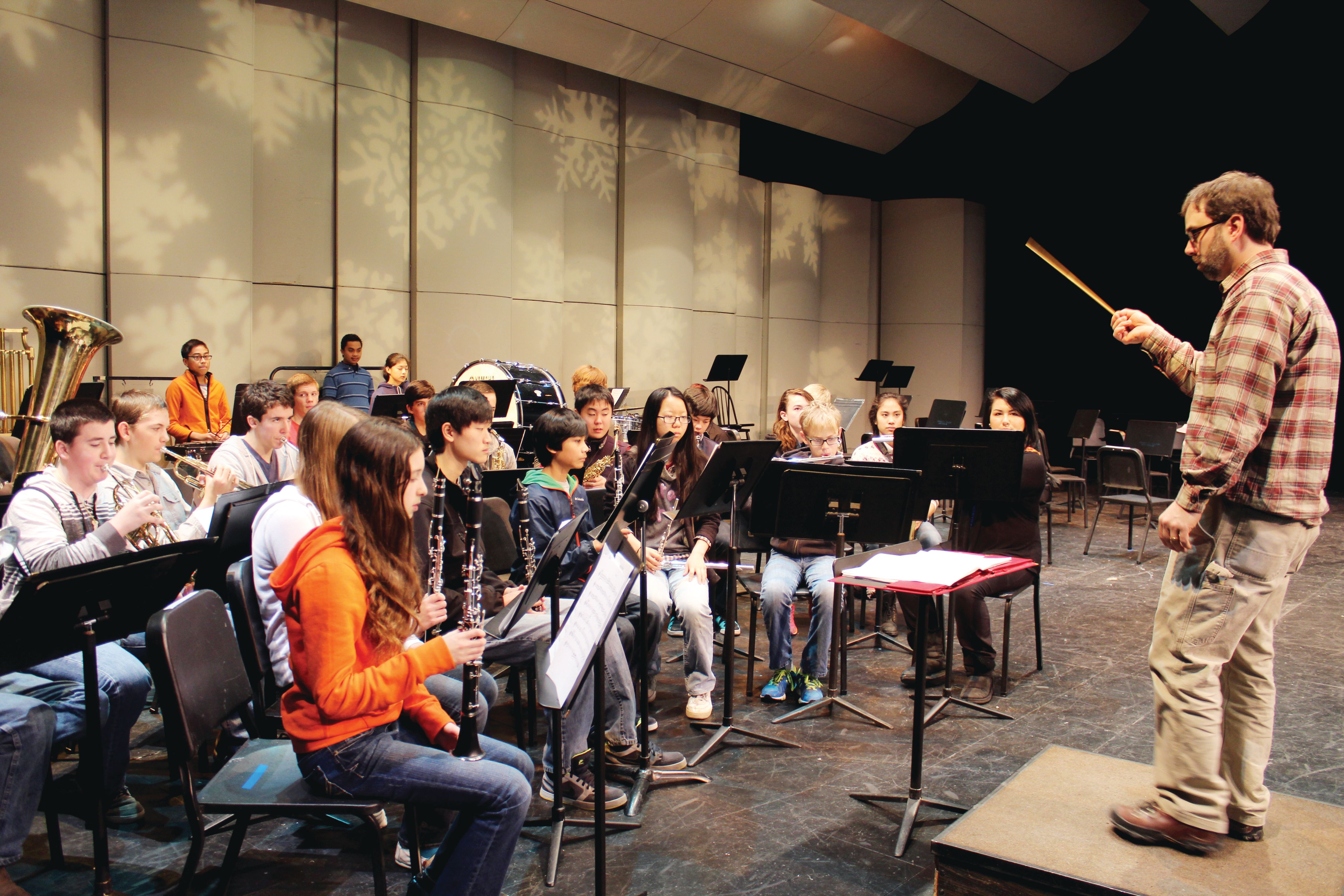 A conductor with a baton leads seated student musicians in a school auditorium.