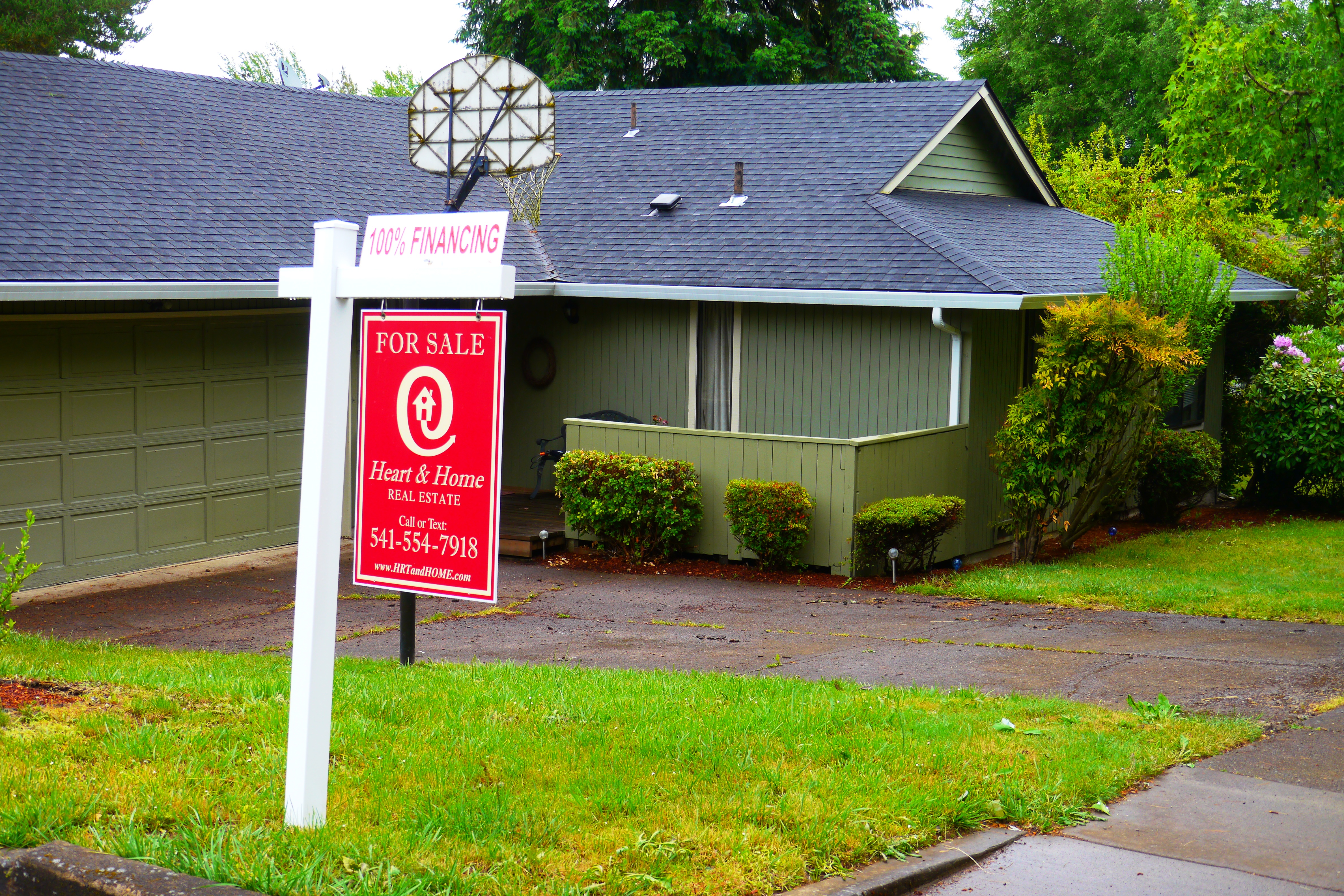 A real estate for-sale sign in front of a single-family home with a green lawn.