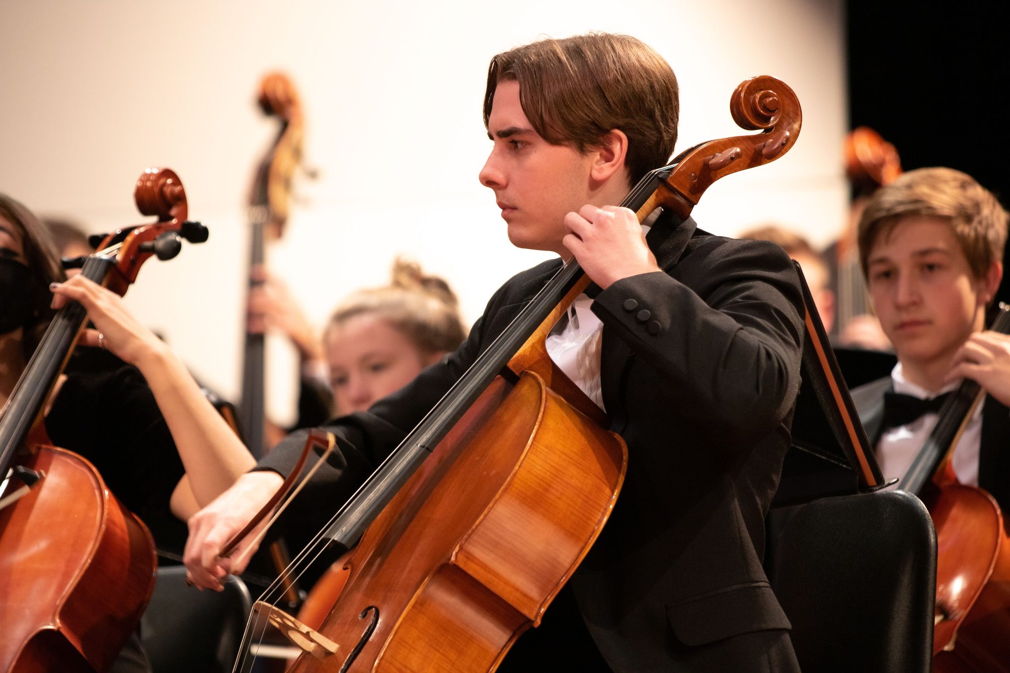 Focused young cellist playing during an orchestra performance indoors.