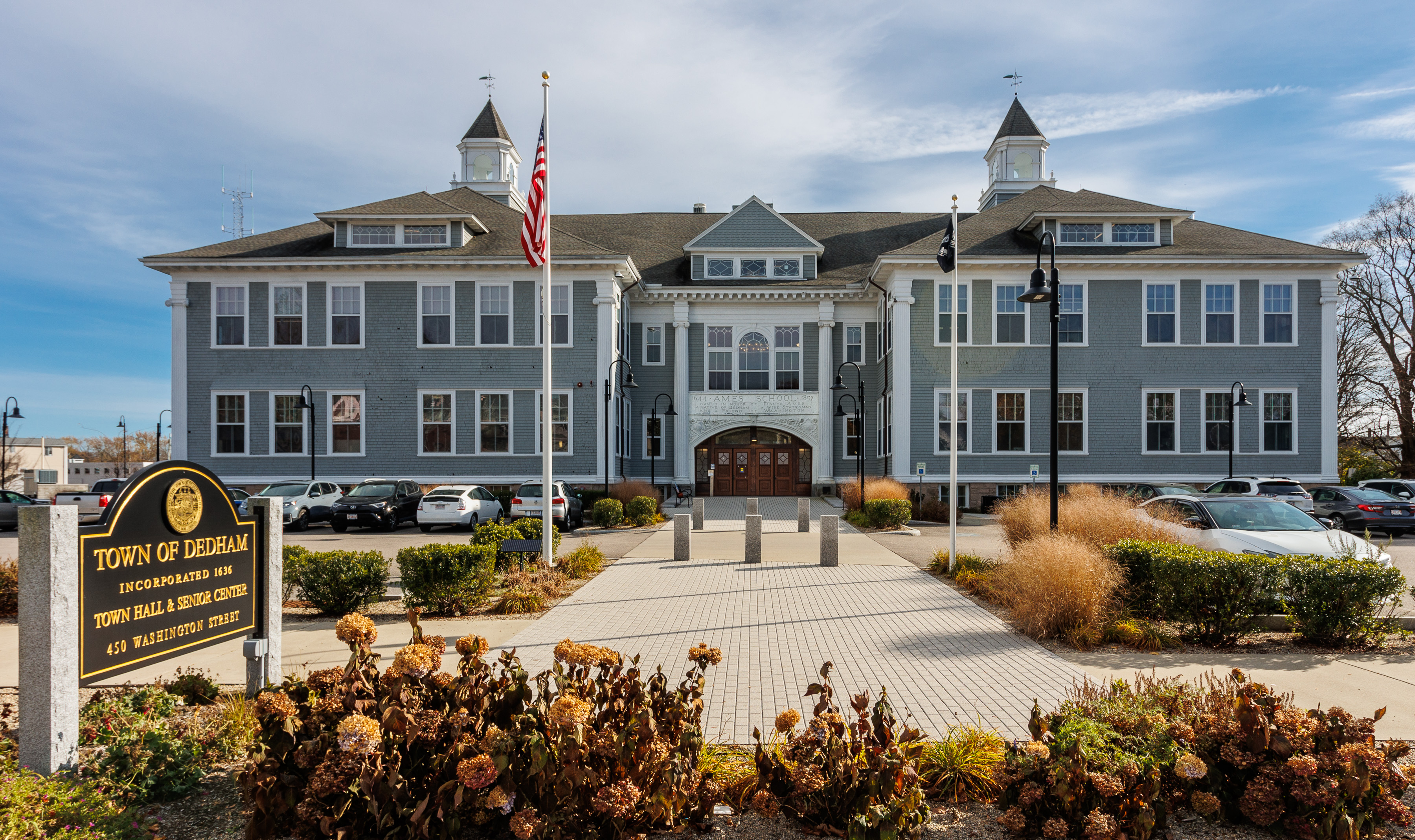 Gray colonial-style town hall building with two white cupolas and an American flag.