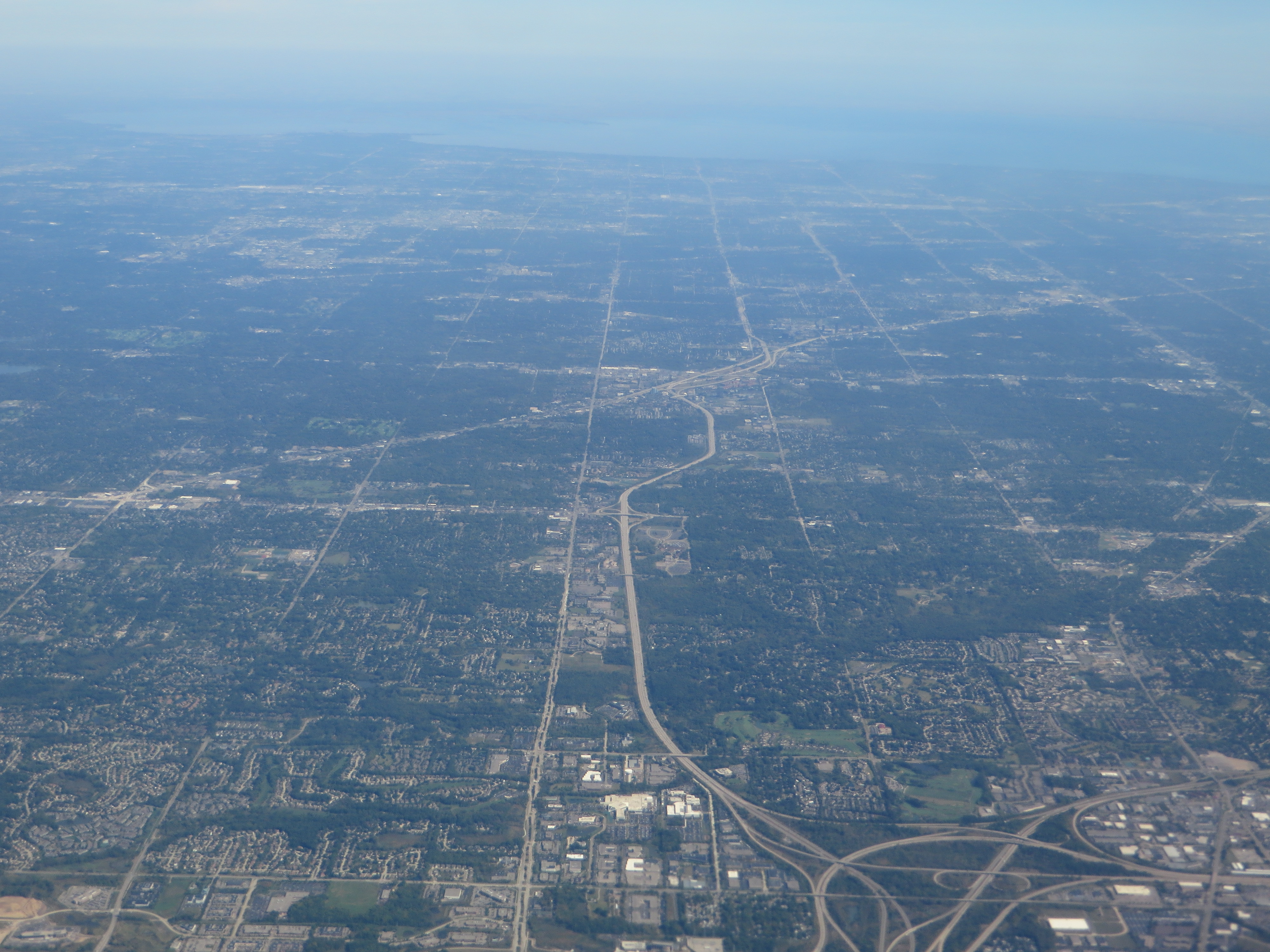 Aerial view of a multi-lane interstate freeway with interchange ramps through suburban Michigan.