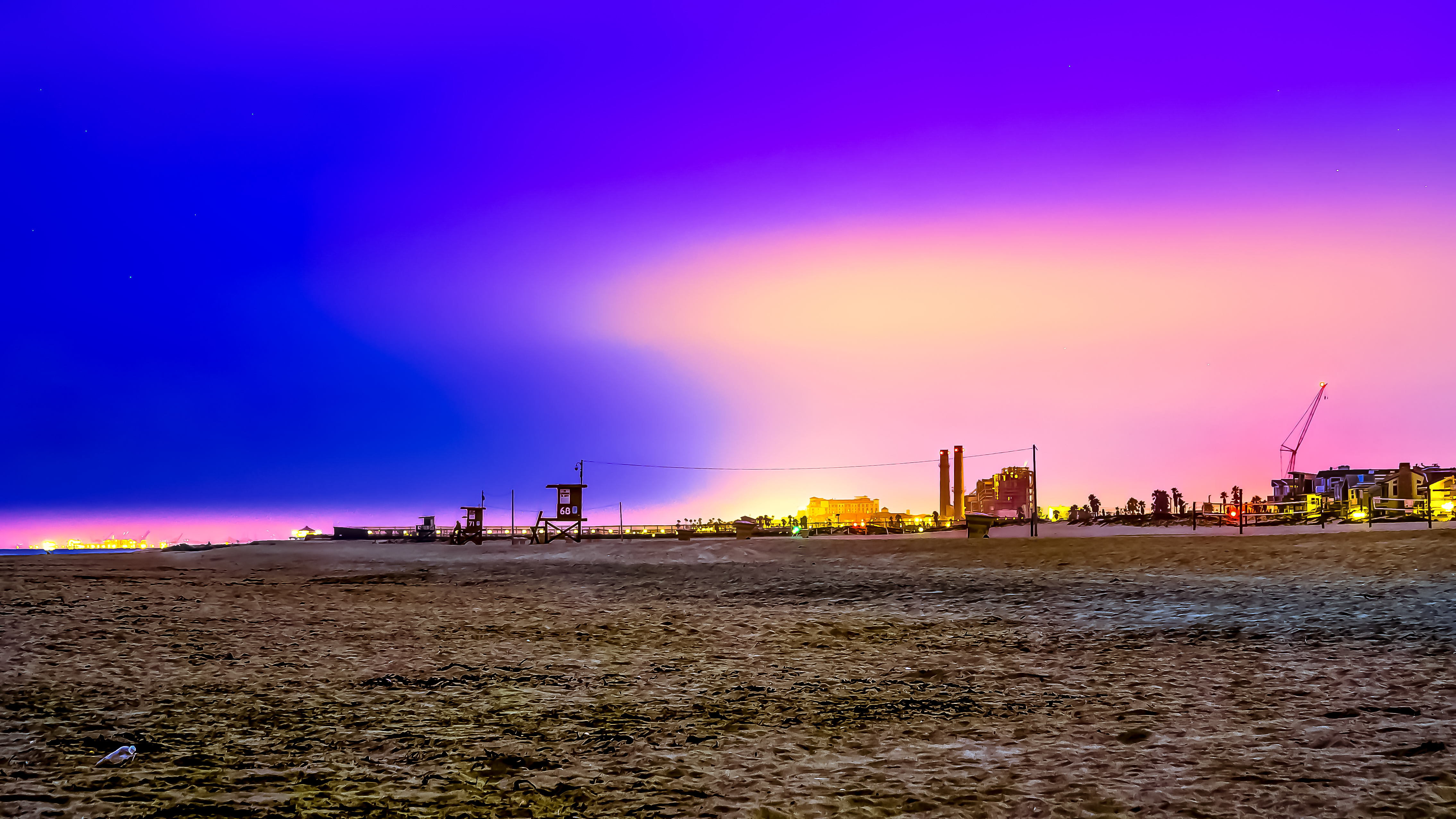 Sandy beach at dusk with a lifeguard tower silhouetted against a colorful sky.