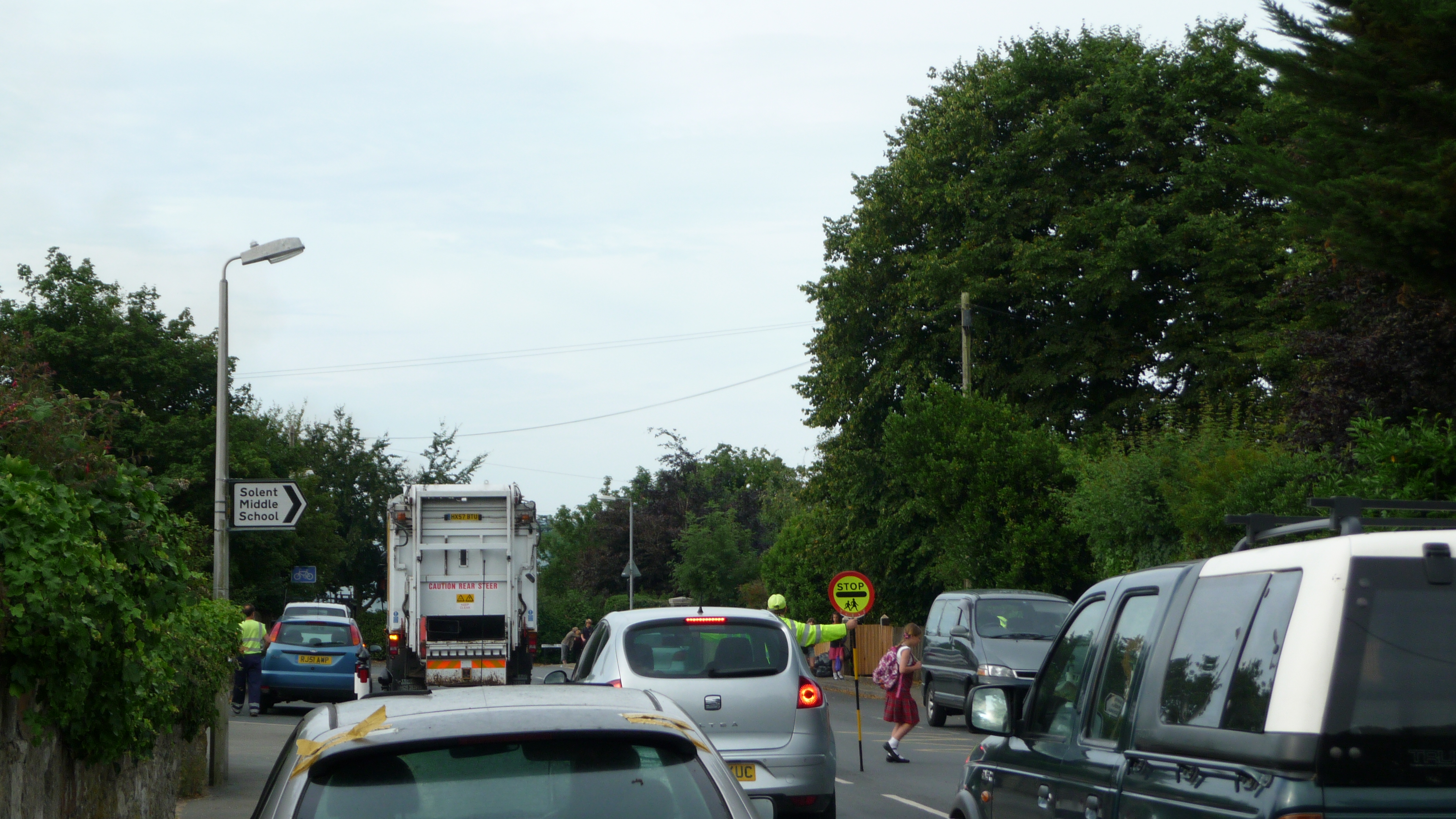 A crossing guard holds a stop sign in a road with cars queued behind.