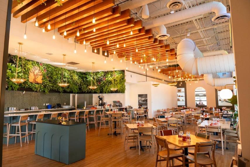 Modern restaurant interior with a living green wall behind a bar and wood-slat ceiling.