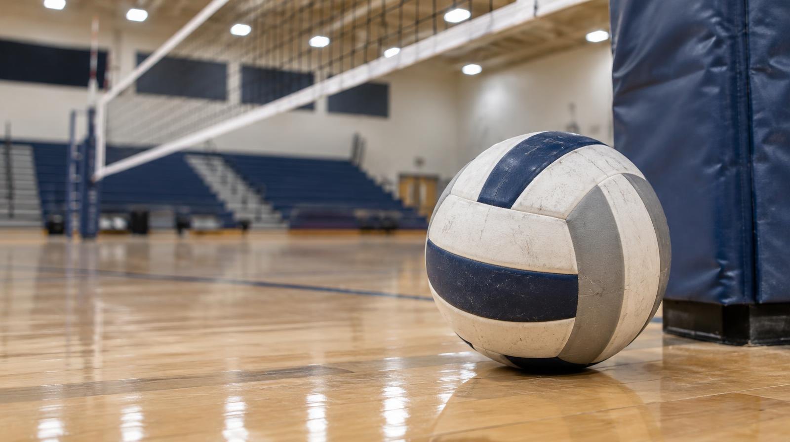 A volleyball resting on a hardwood gymnasium floor near the net post.