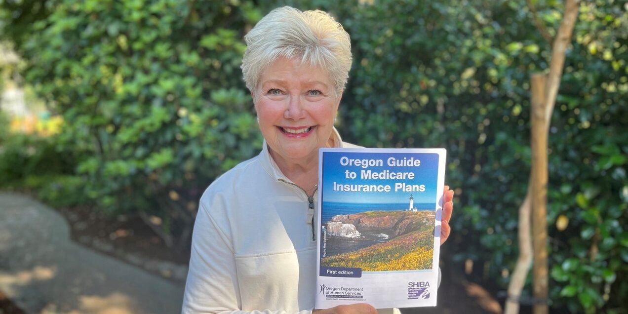 Smiling older woman holding an Oregon Medicare insurance guide booklet outdoors.