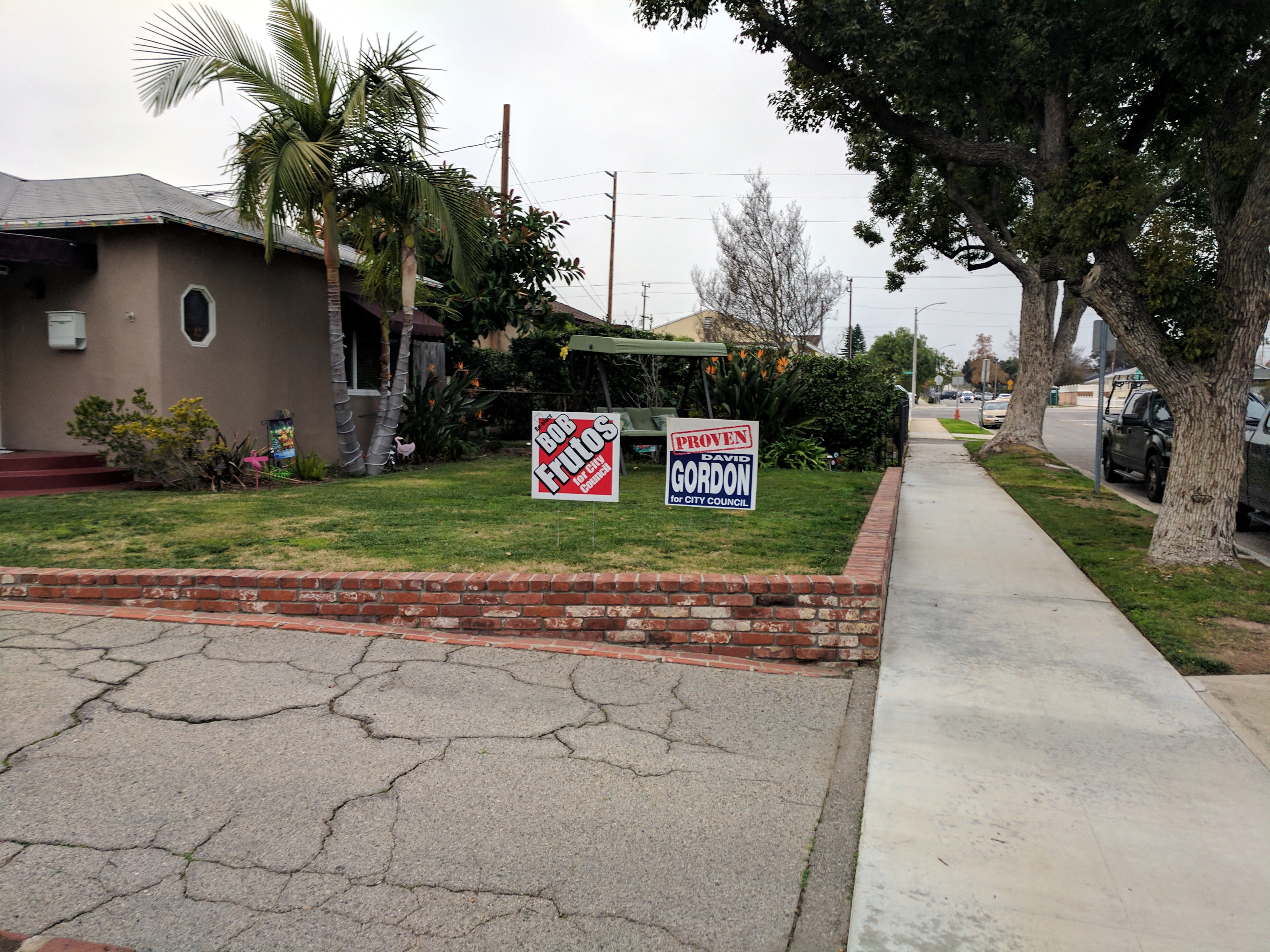 Two campaign yard signs planted in a green residential lawn near a sidewalk.