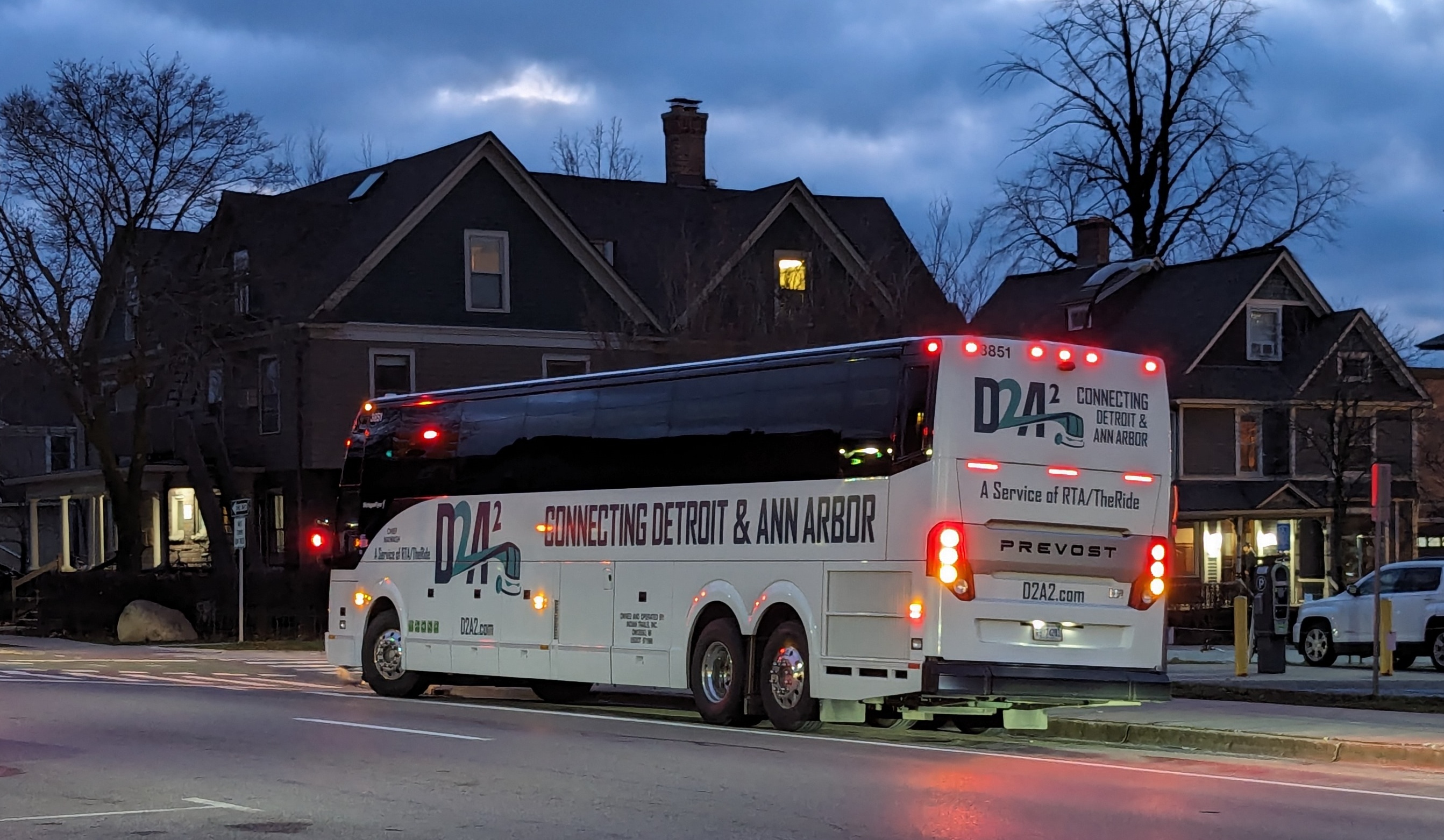 A white coach bus with TheRide branding stopped at a transit center at dusk.