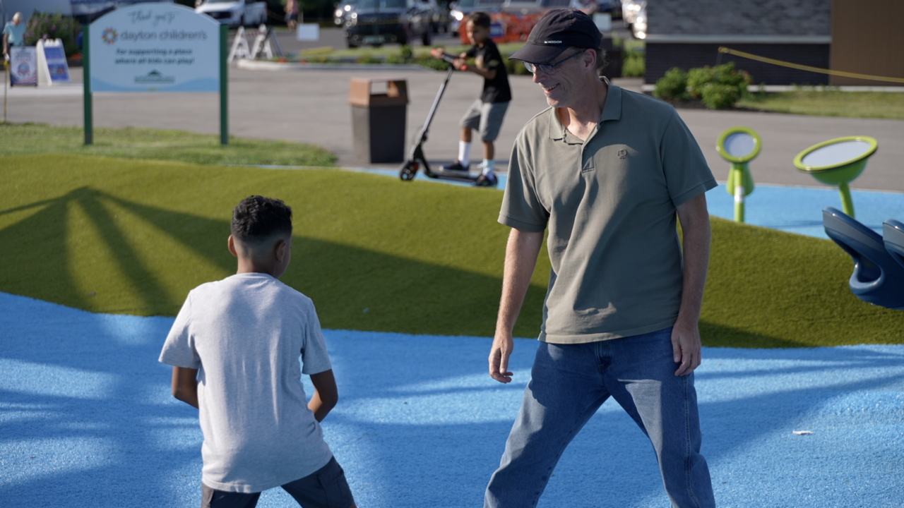 An adult man and a young boy stand together on a colorful playground surface.