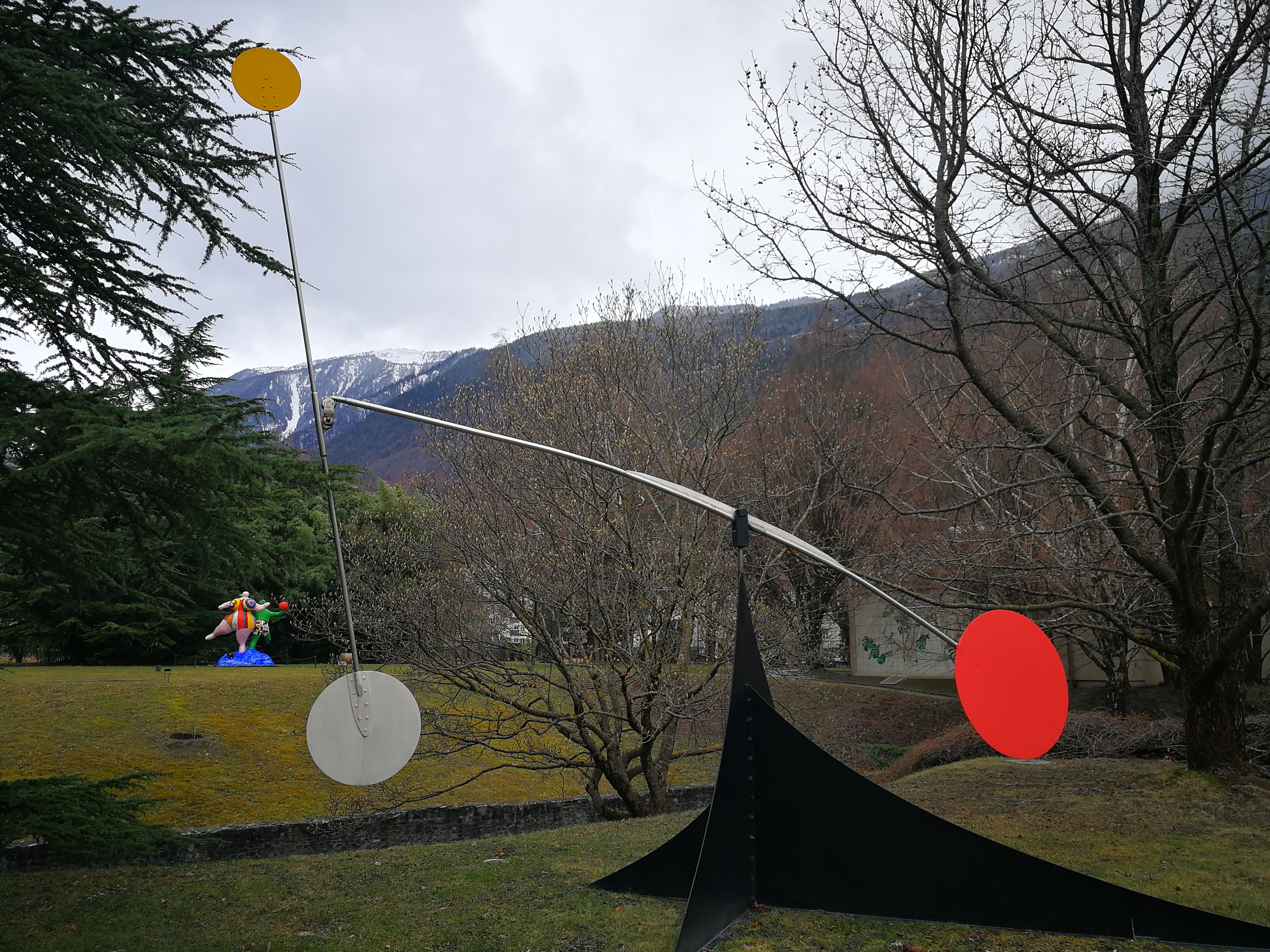 Large metal sculpture with yellow, white, and red circular discs in an outdoor sculpture garden.