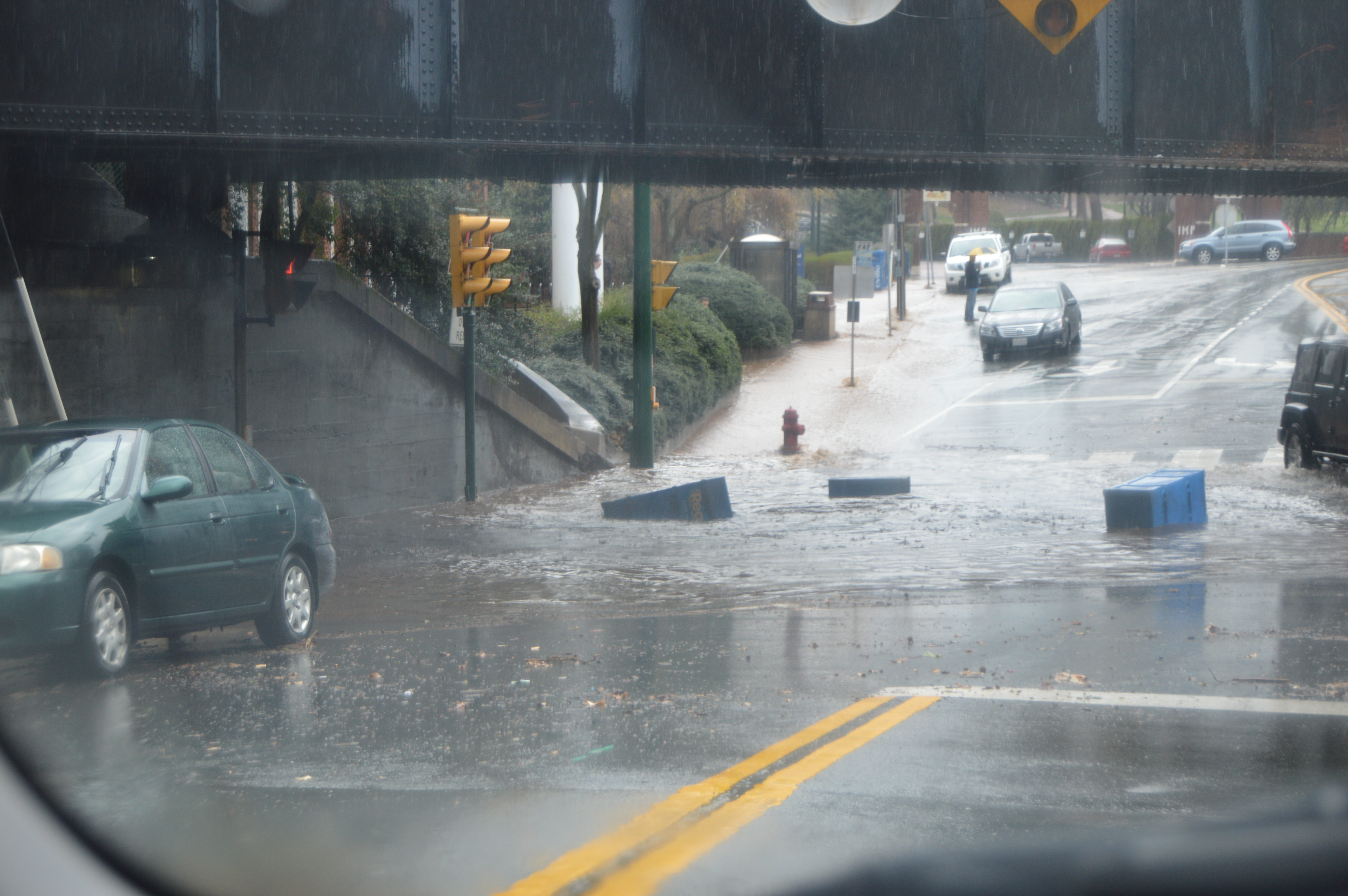 A flooded urban intersection with vehicles navigating fast-moving floodwaters.