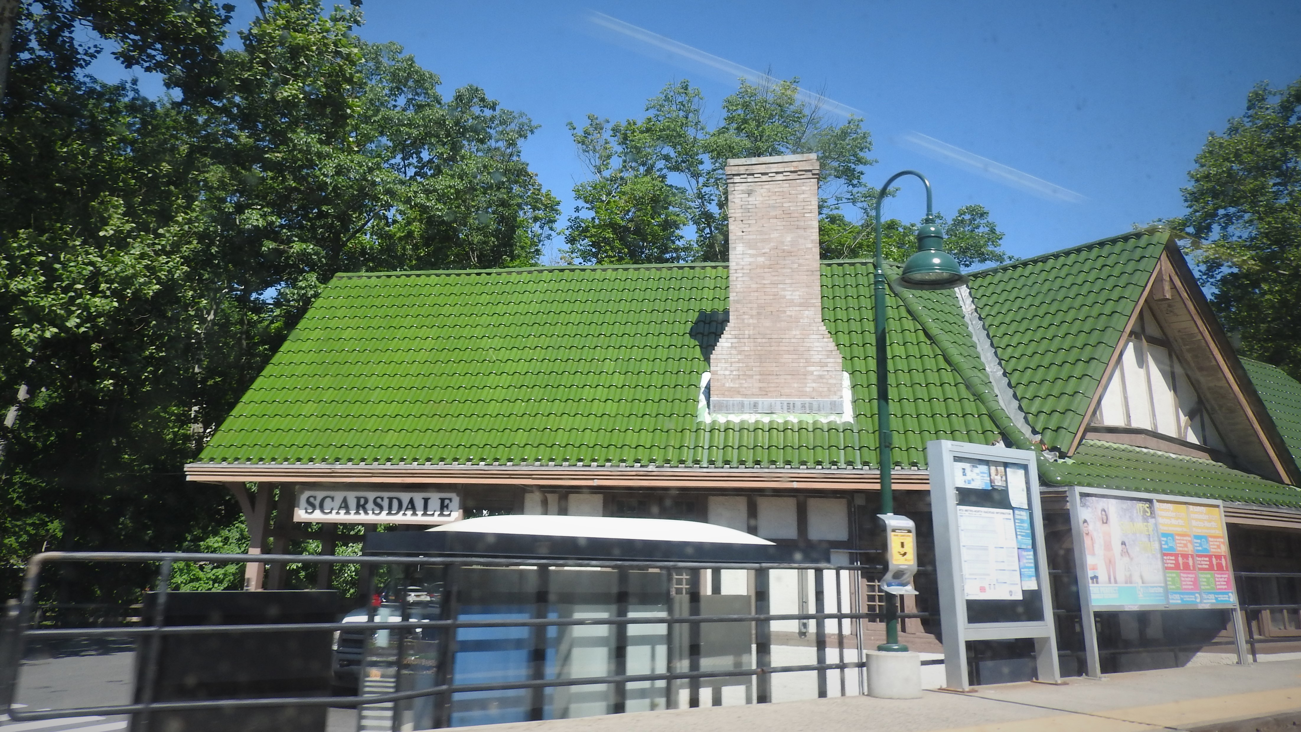 Scarsdale train station building with green tiled roof and station sign.