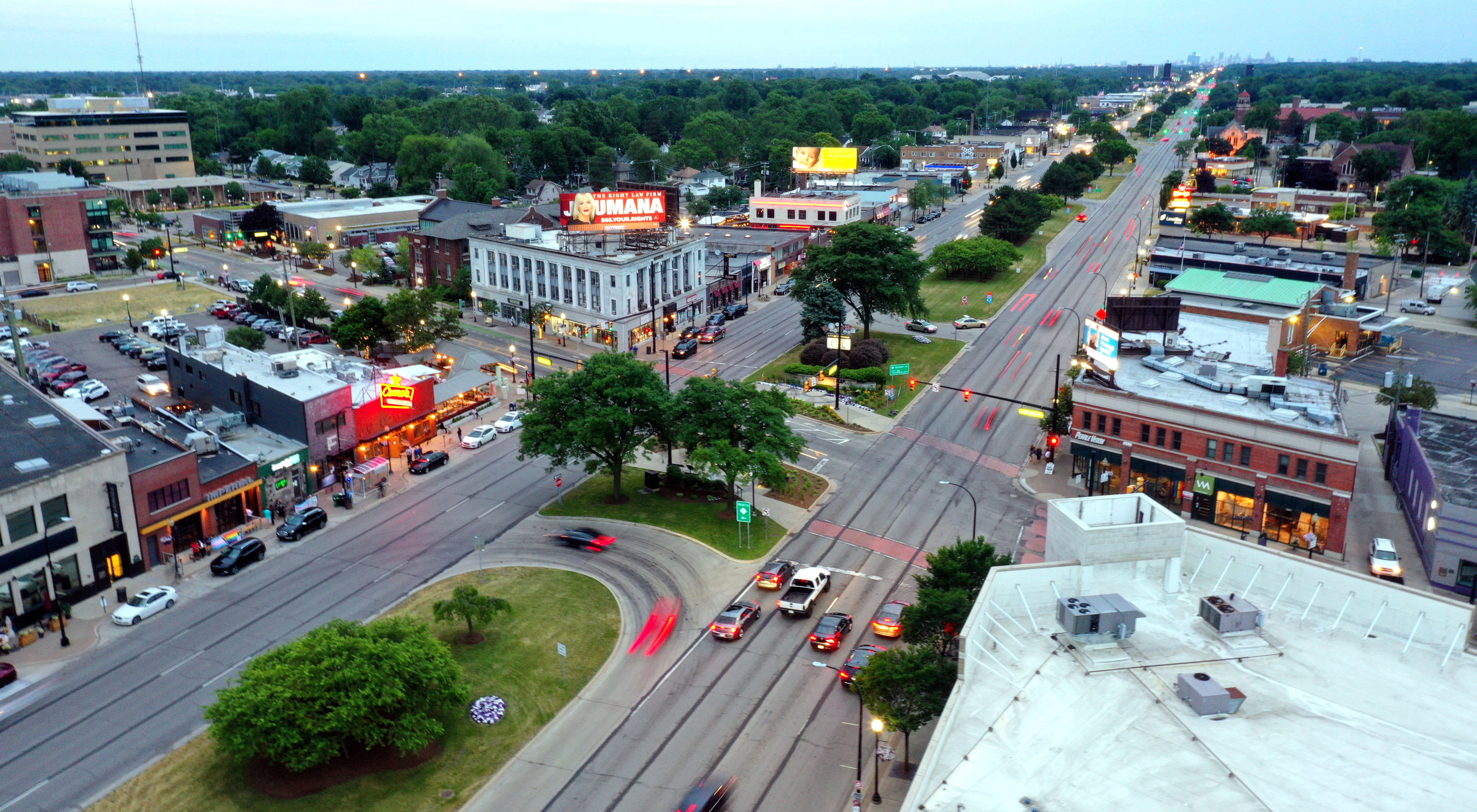 Aerial dusk view of a busy urban intersection lined with commercial buildings and trees.