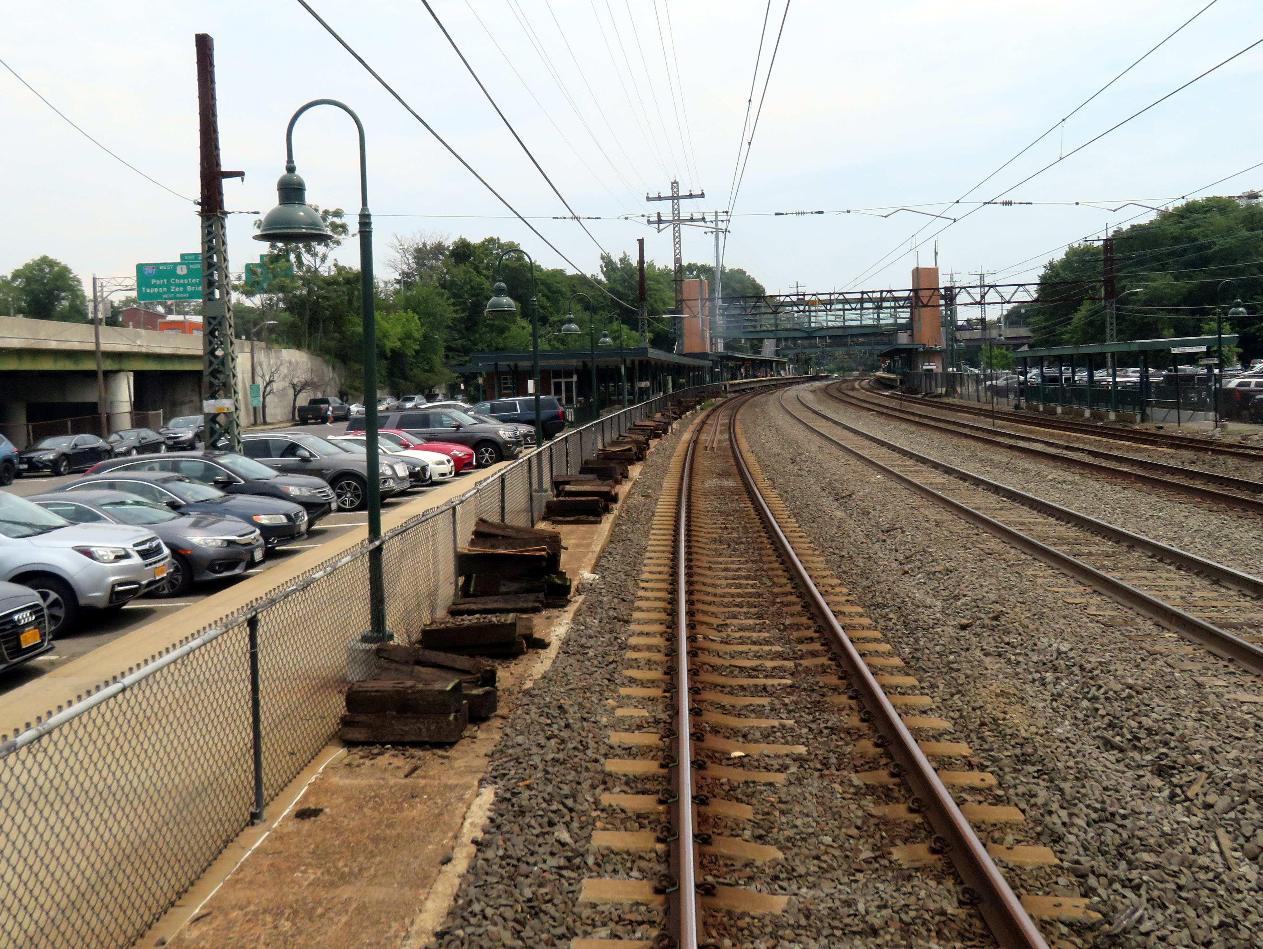 Railroad platform and curved tracks at Rye station, with a large surface parking lot alongside.