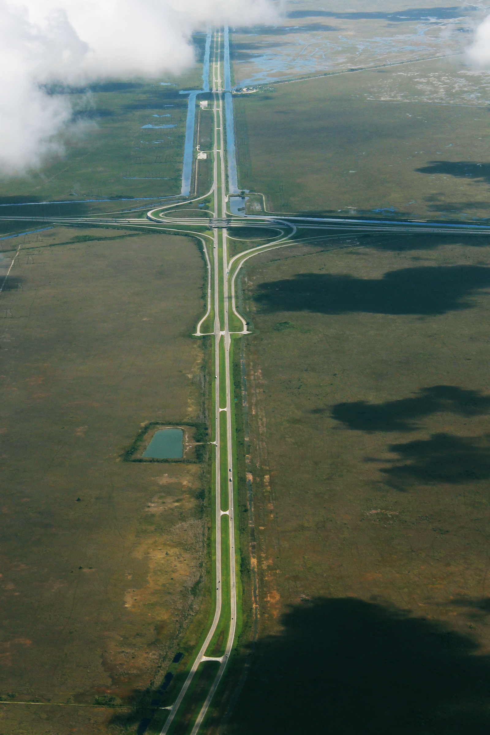 Aerial view of a divided highway through flat marshy terrain with a diamond interchange.