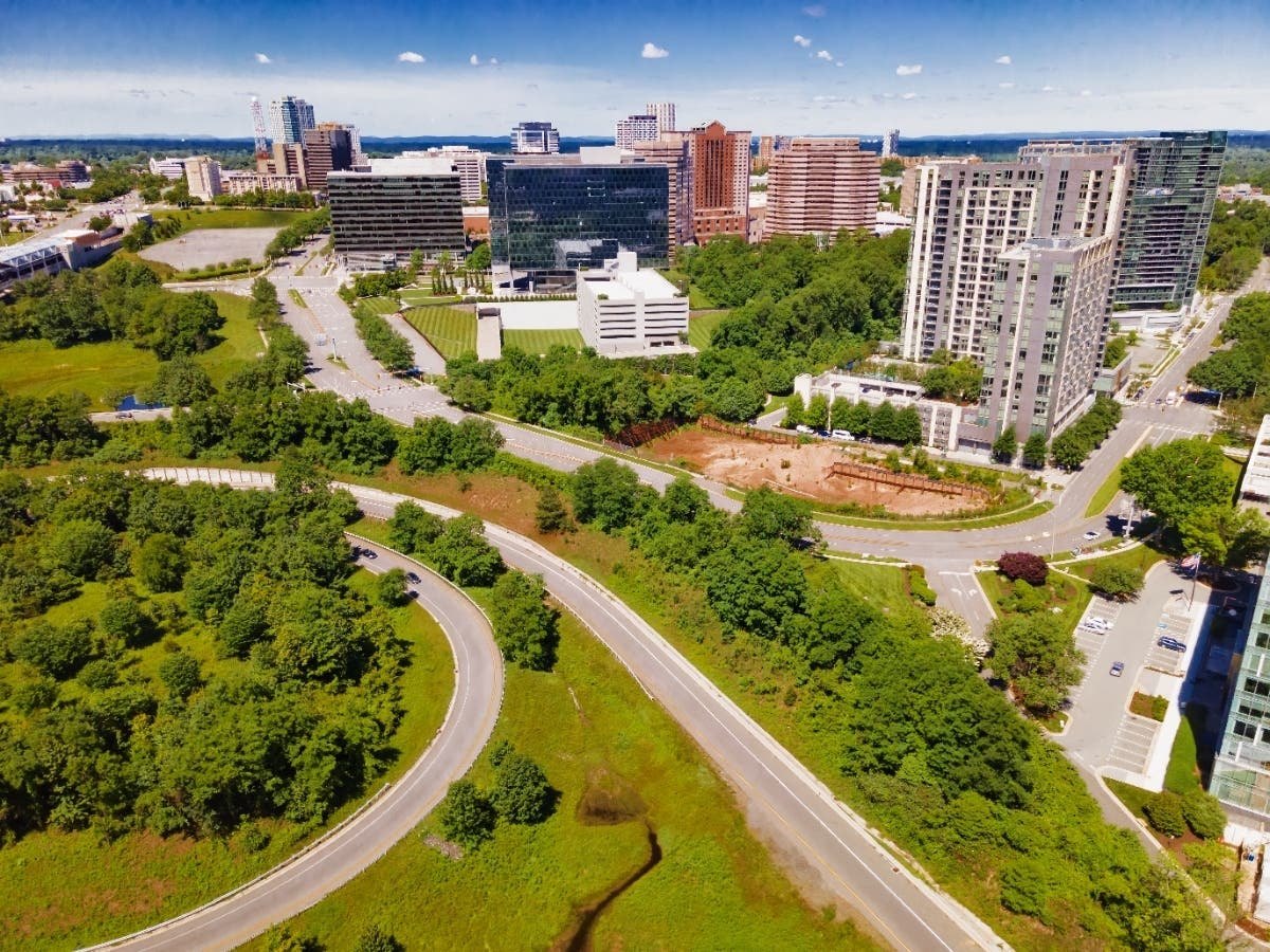Aerial view of high-rise buildings, curving roads, green spaces, and a construction site in a suburban area.