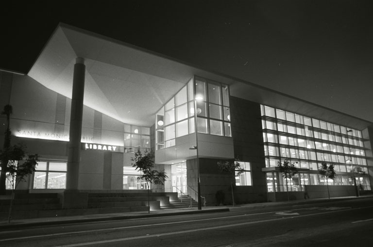Exterior night view of a modernist public library building with large illuminated glass windows.
