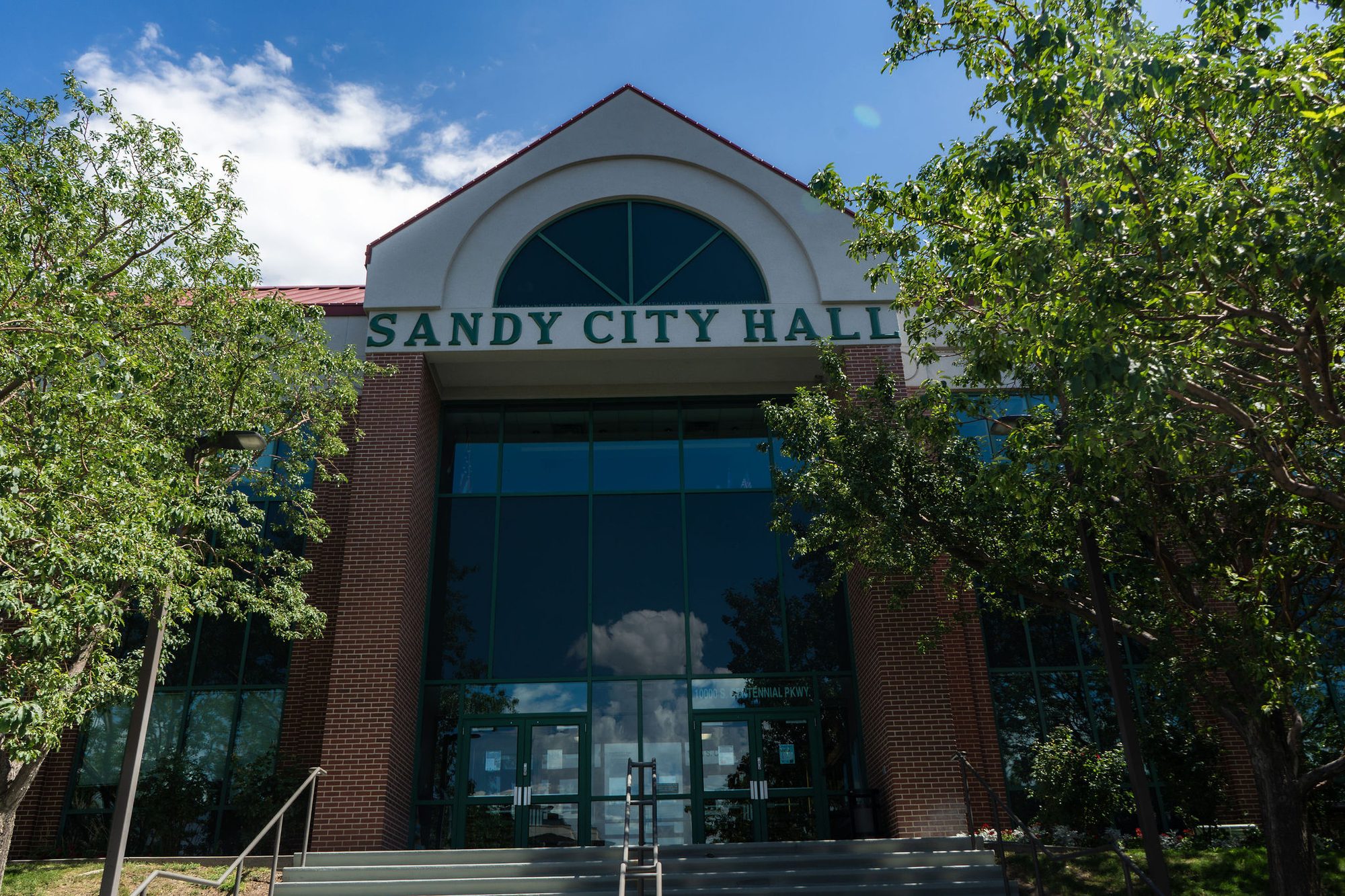 Brick city hall building with arched entrance and large tinted-glass facade.