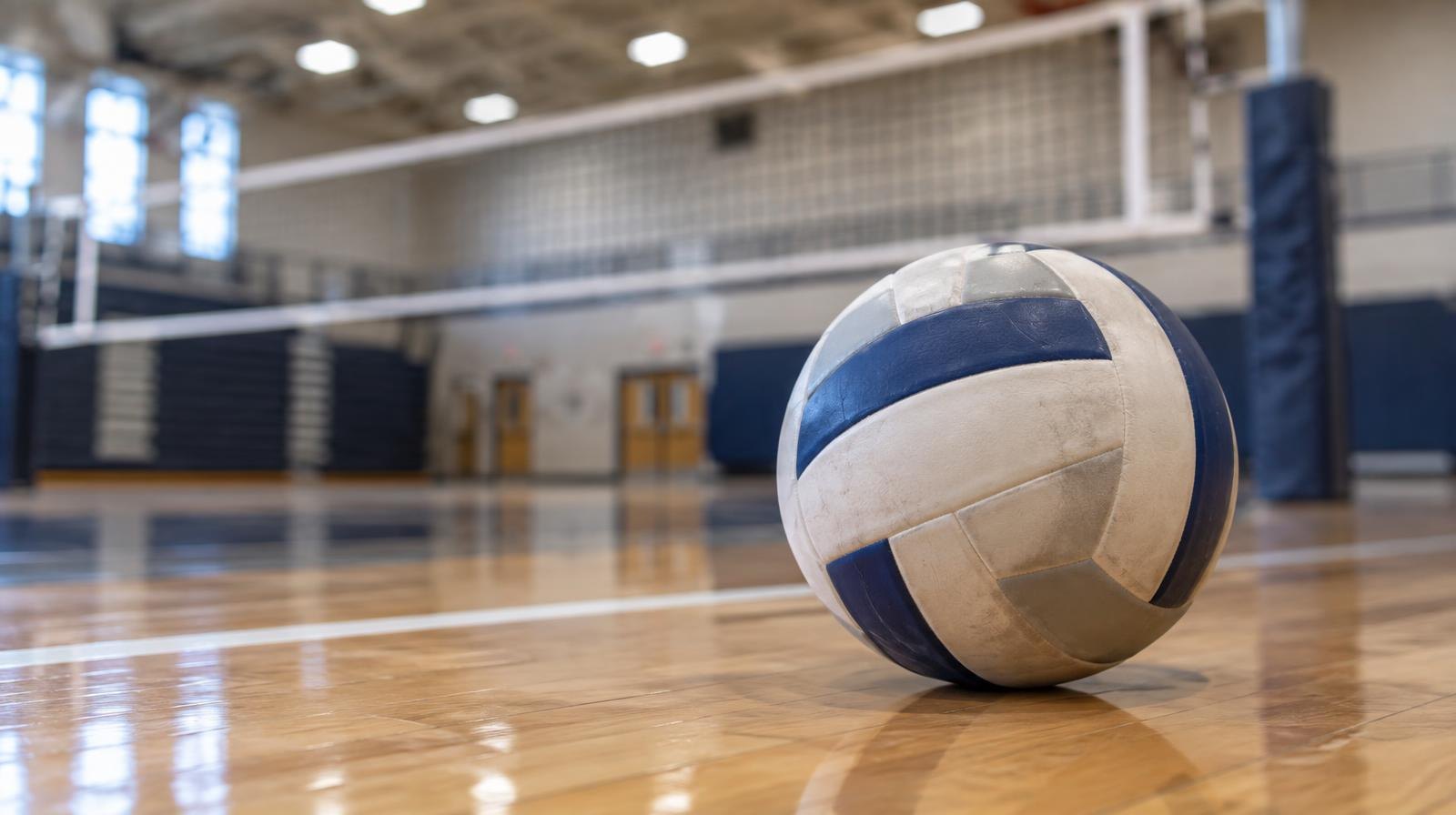 A volleyball resting on a hardwood gym floor near a net.