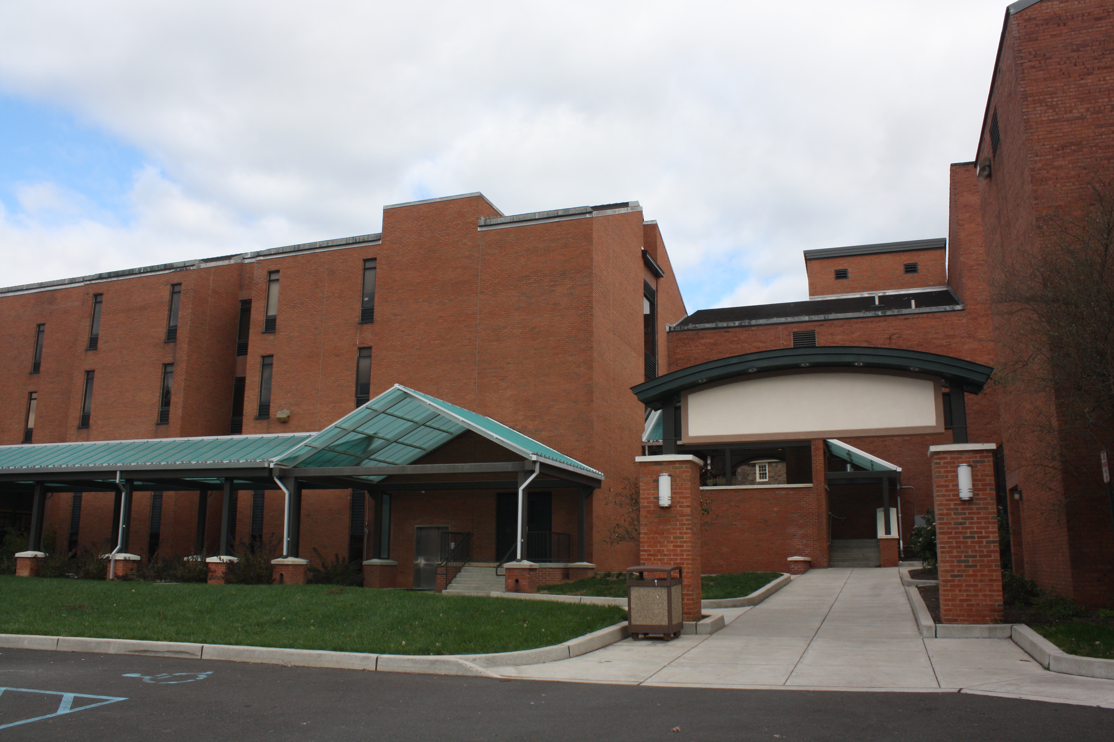 Multi-story red brick college building with a green-roofed covered walkway entrance.