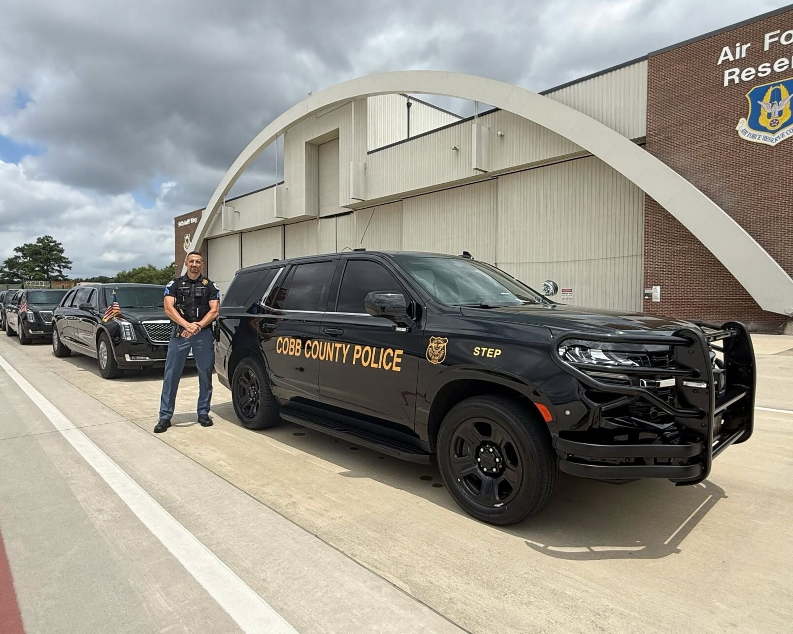 Uniformed officer standing next to a marked Cobb County Police SUV at an Air Force Reserve facility.