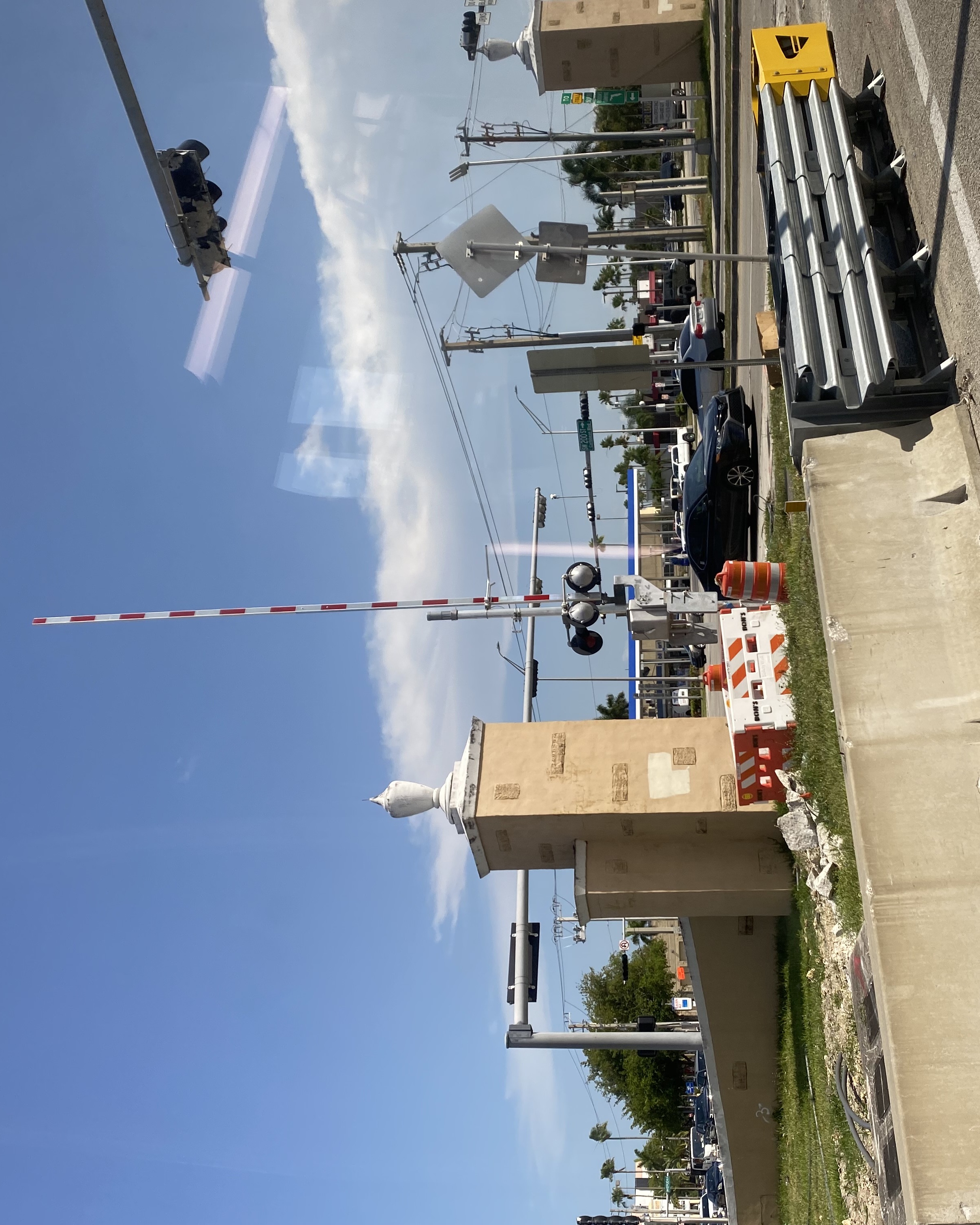 A lowered gate arm at a road intersection with traffic signals and palm trees in the background.