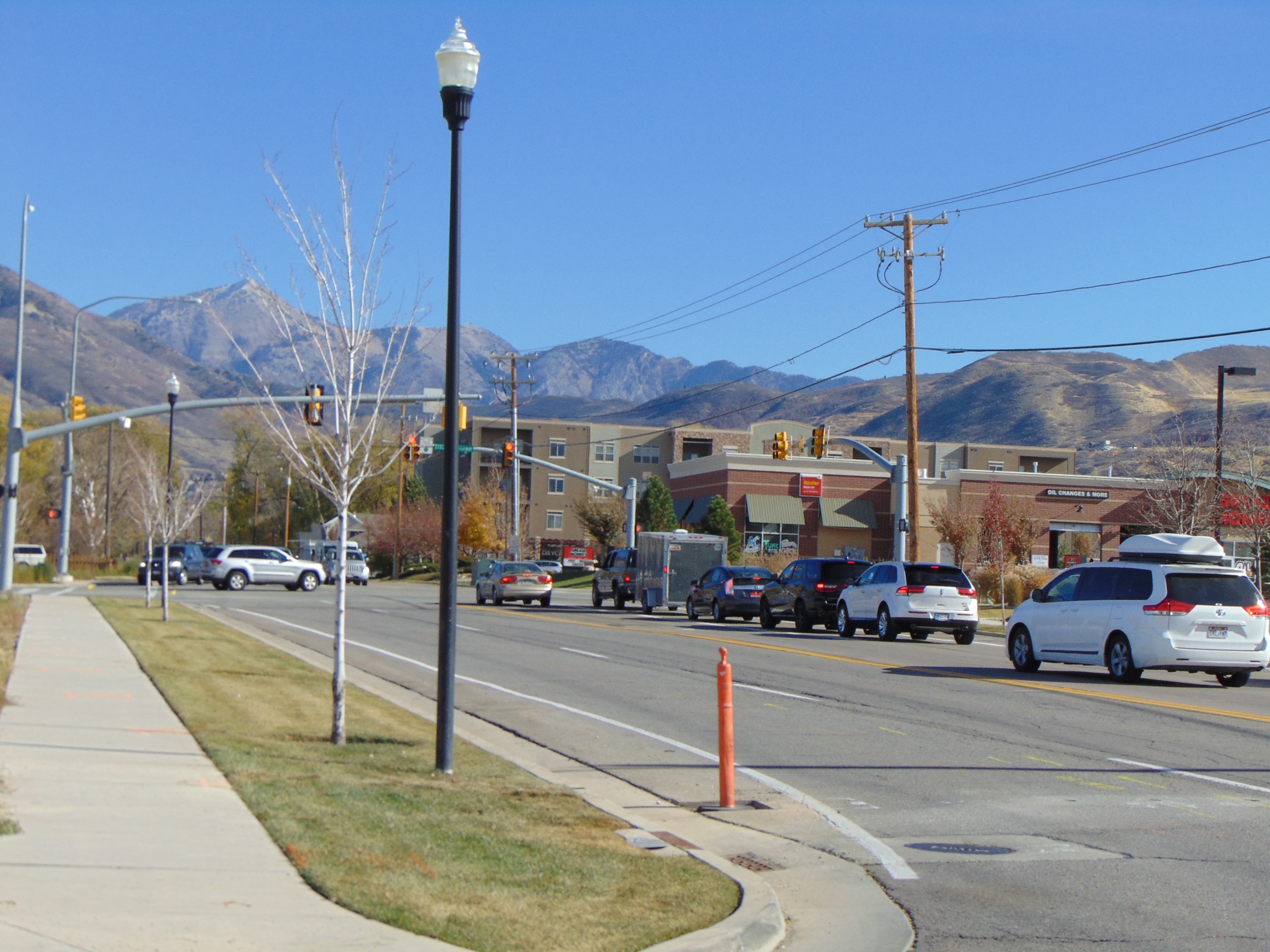 Multi-lane road with vehicles, traffic lights, commercial buildings, and mountains in the background.