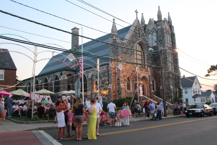 Crowd gathered outside a large stone church at an outdoor evening festival with string lights.