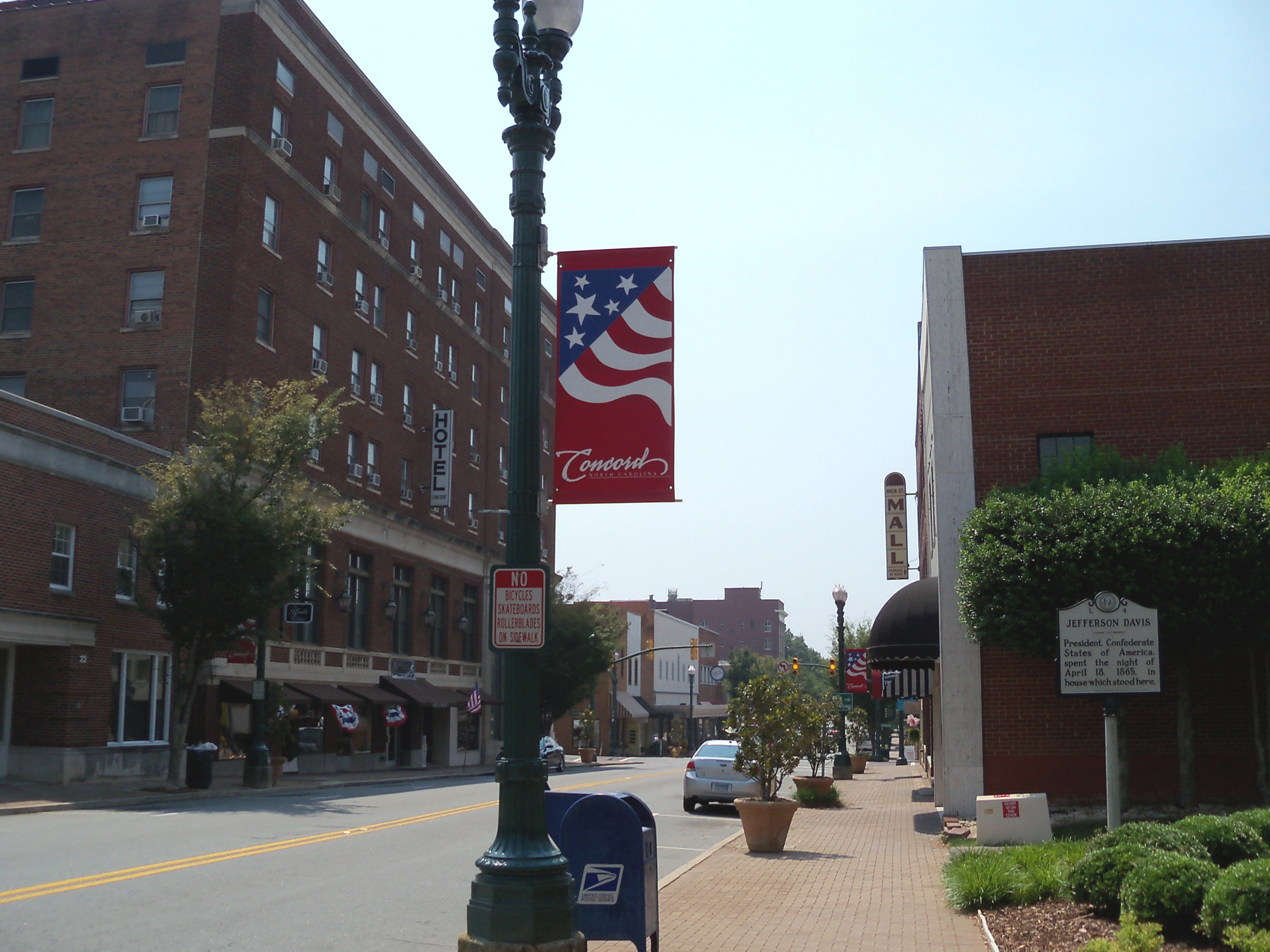 Downtown street with brick buildings, a lamp post bearing a Concord banner, and parked cars.