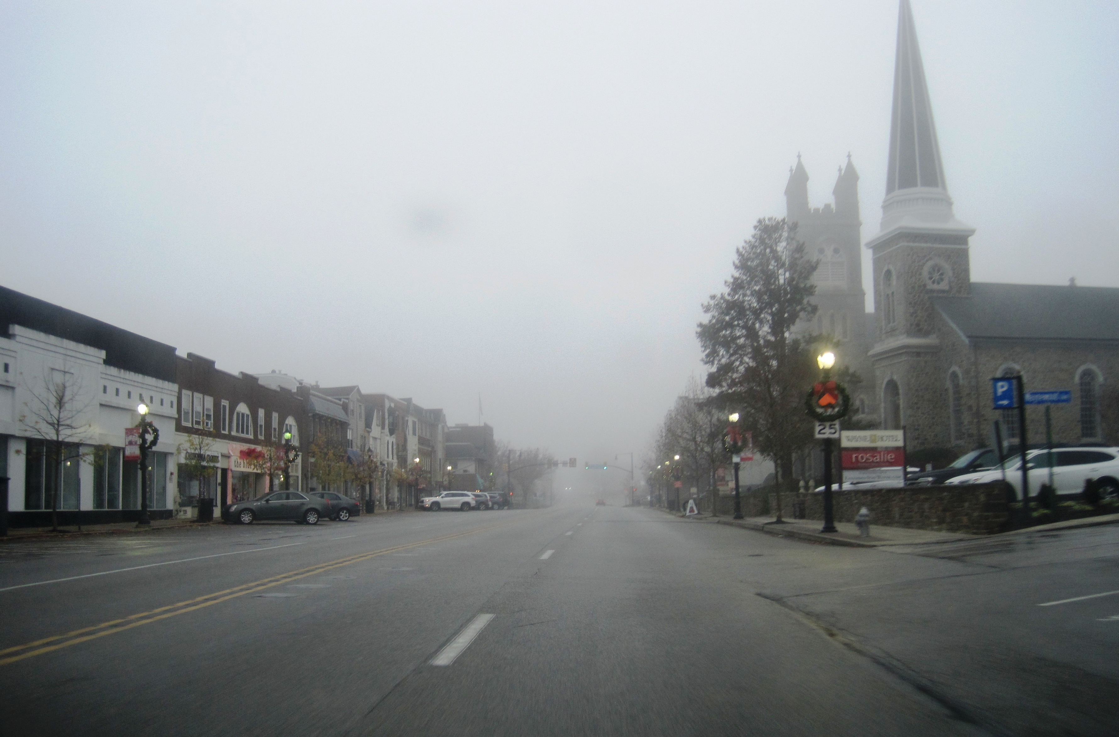 Foggy view looking west along Lancaster Avenue in Wayne with traffic signals and commercial buildings.