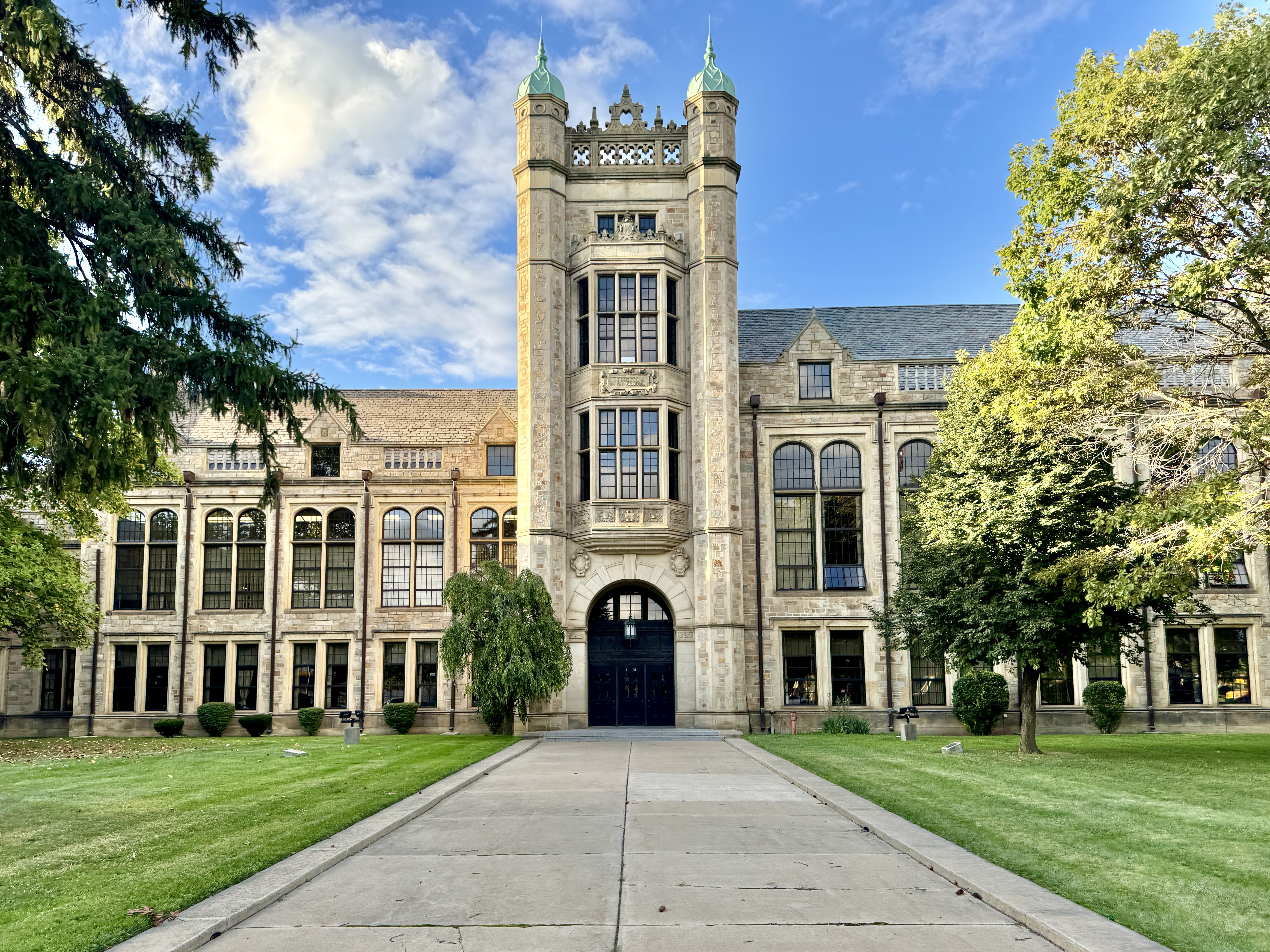 Exterior of a large stone high school building with a central tower and copper-capped cupolas.