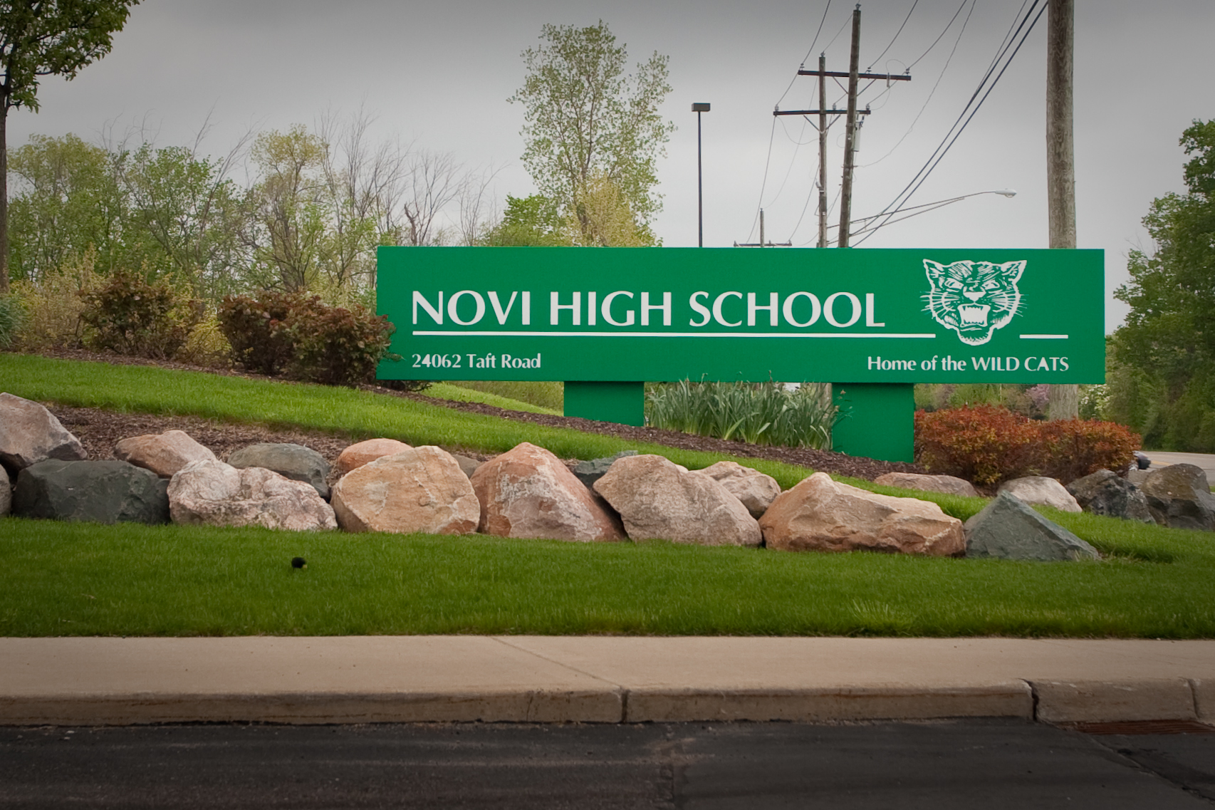 Green entrance sign for Novi High School surrounded by decorative boulders and landscaping.