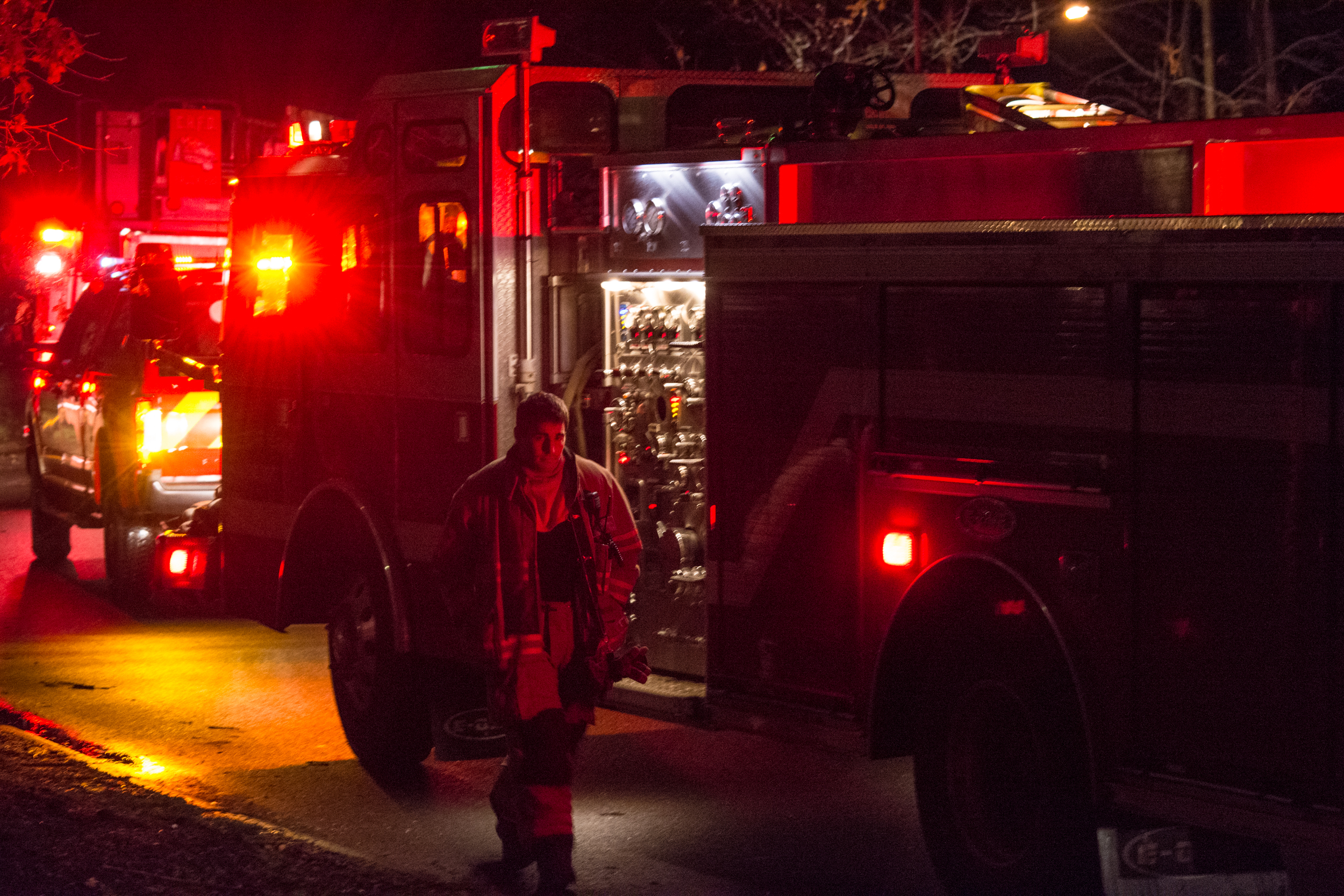 A firefighter walking between fire trucks at night with emergency lights illuminated.