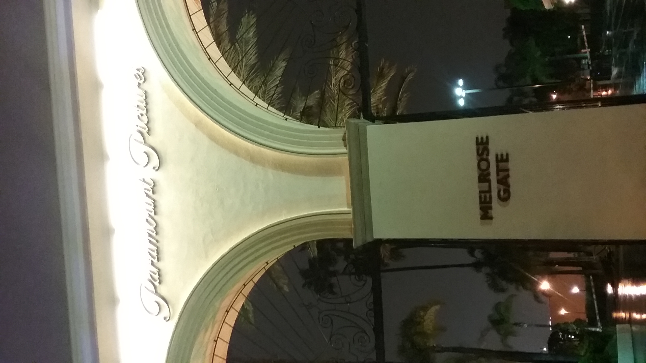 Illuminated Paramount Pictures entrance gate at night with palm trees visible through iron gates