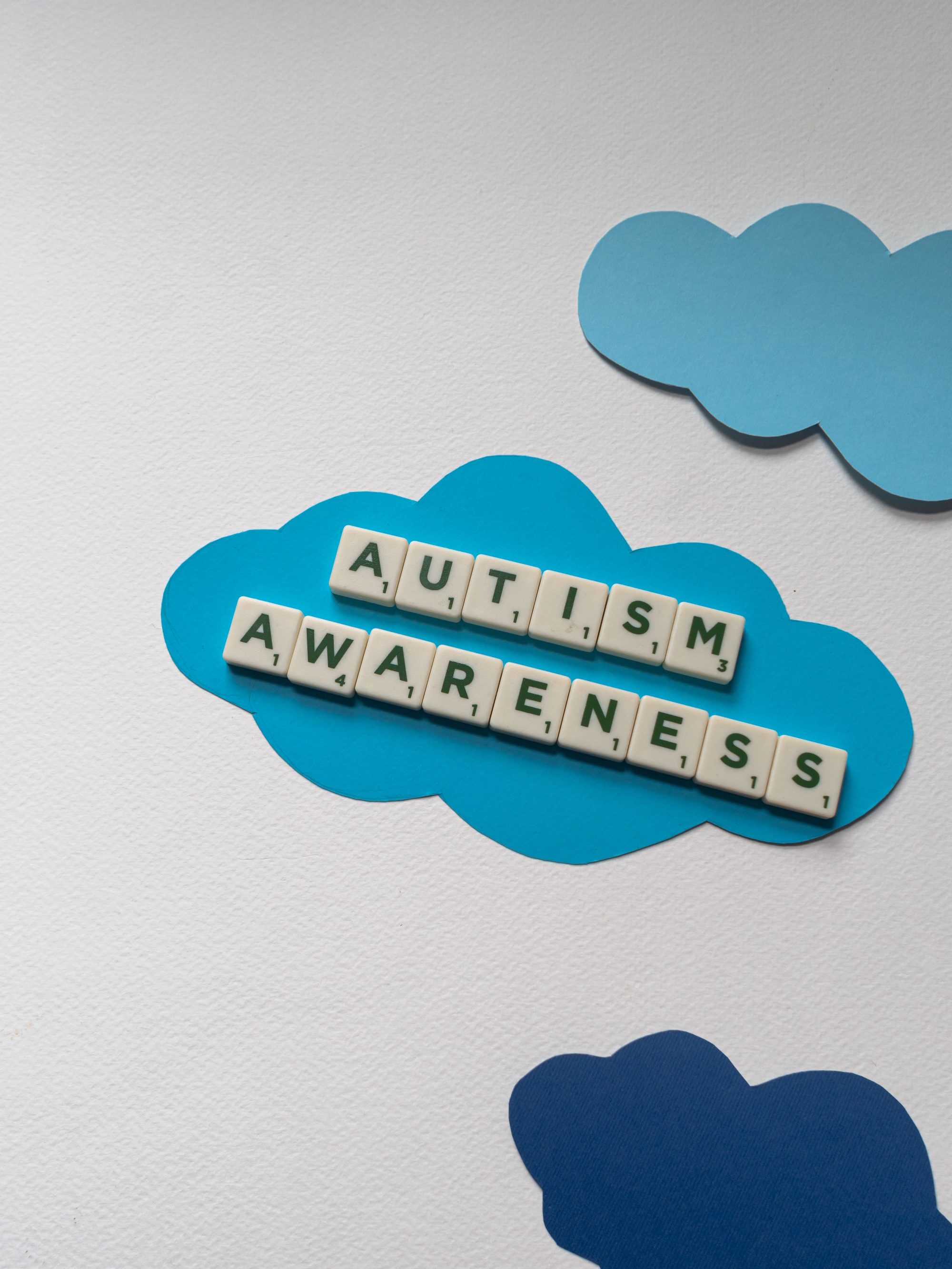 Autism awareness message displayed with letter tiles against paper clouds background.