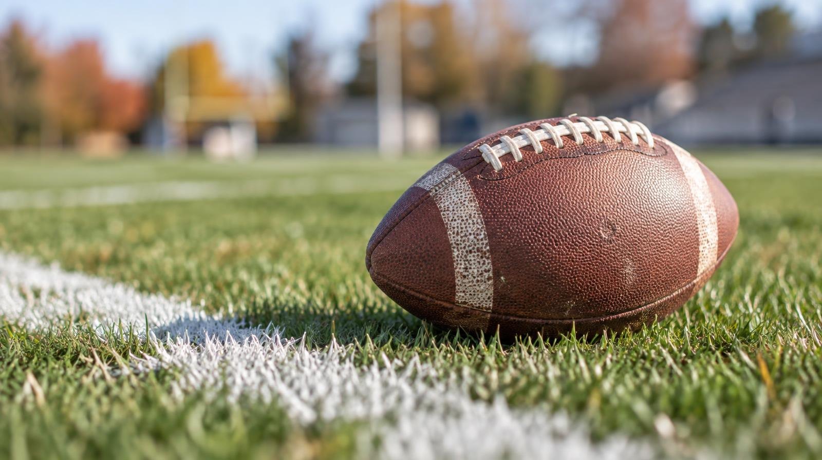 An American football resting on green grass beside a white painted yard line.