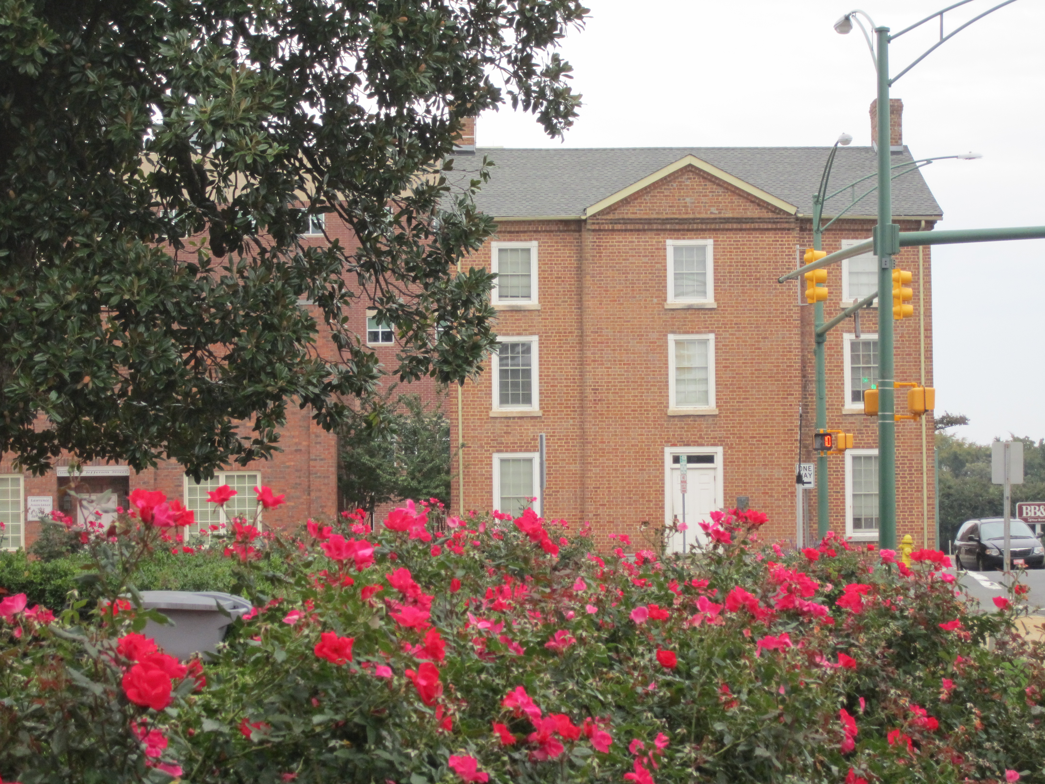 Historic red brick building in downtown Monroe, framed by blooming rose bushes.