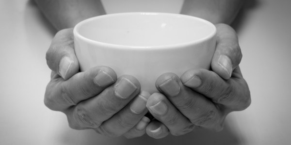 Two hands cupping an empty white ceramic bowl, photographed in black and white.