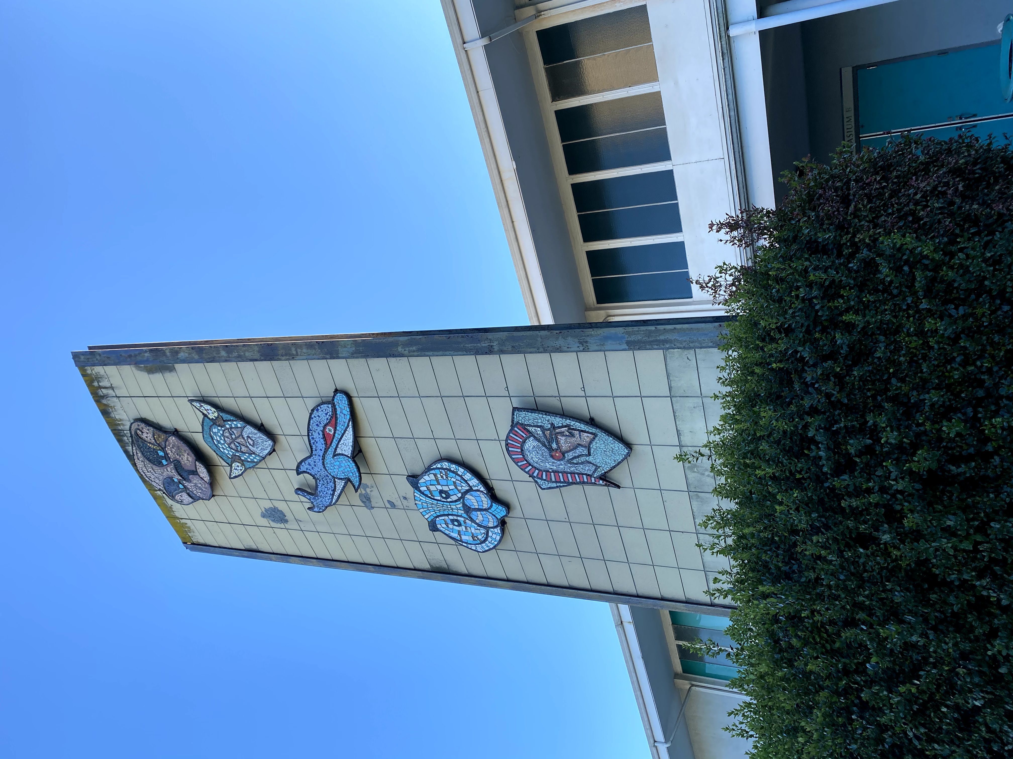 Mid-century modern building tower with five colorful mosaic medallions on a tiled facade.
