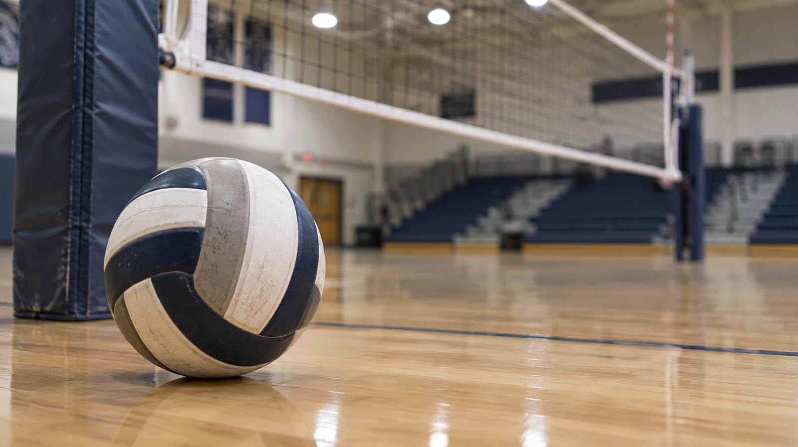 A volleyball resting on a hardwood gymnasium floor near the net post.