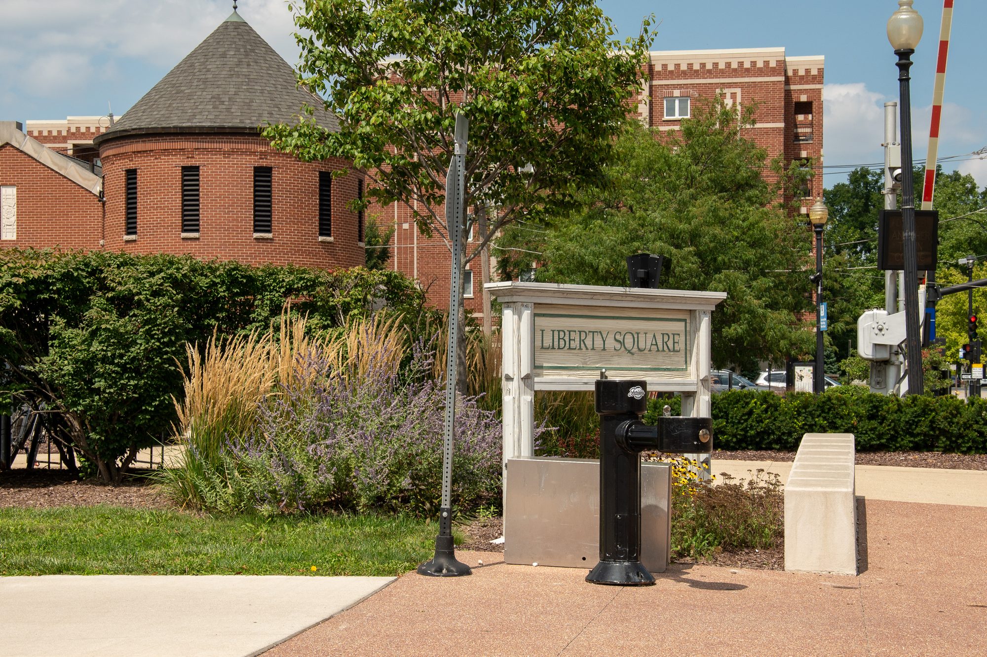 A white Liberty Square sign in a landscaped downtown plaza with brick buildings behind.