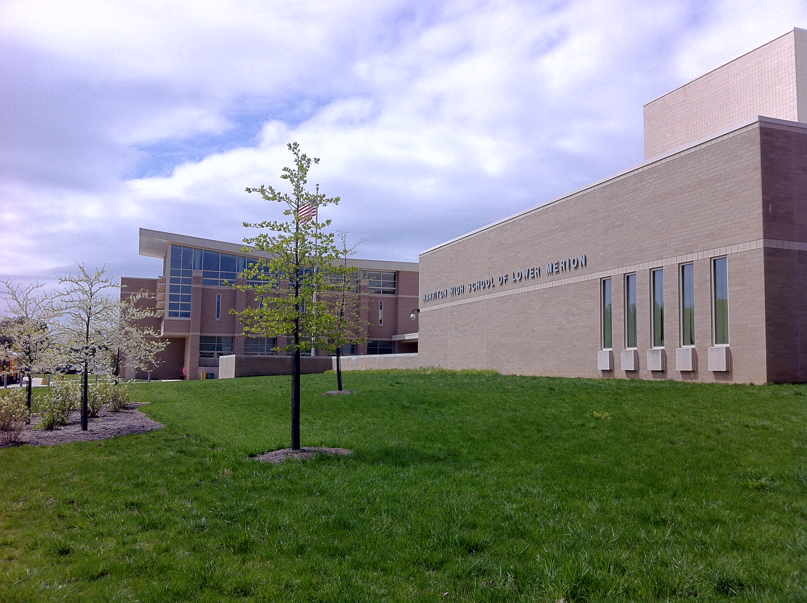 Modern brick and glass high school building with young trees on a cloudy day.