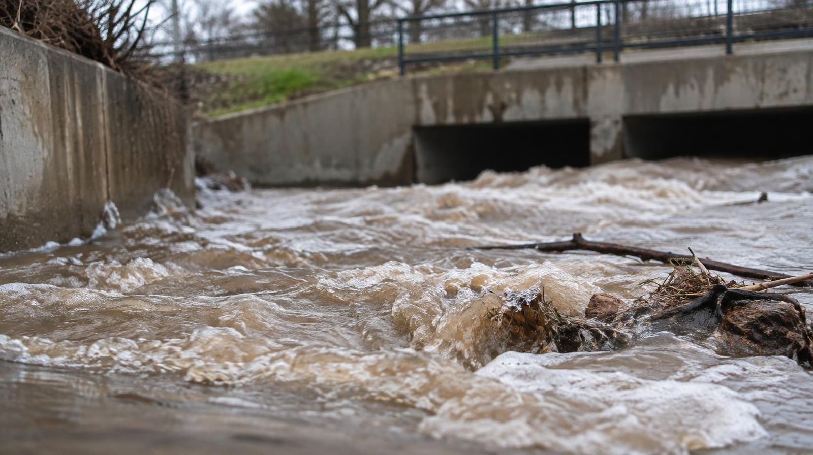 Muddy brown water surges through a concrete drainage channel.