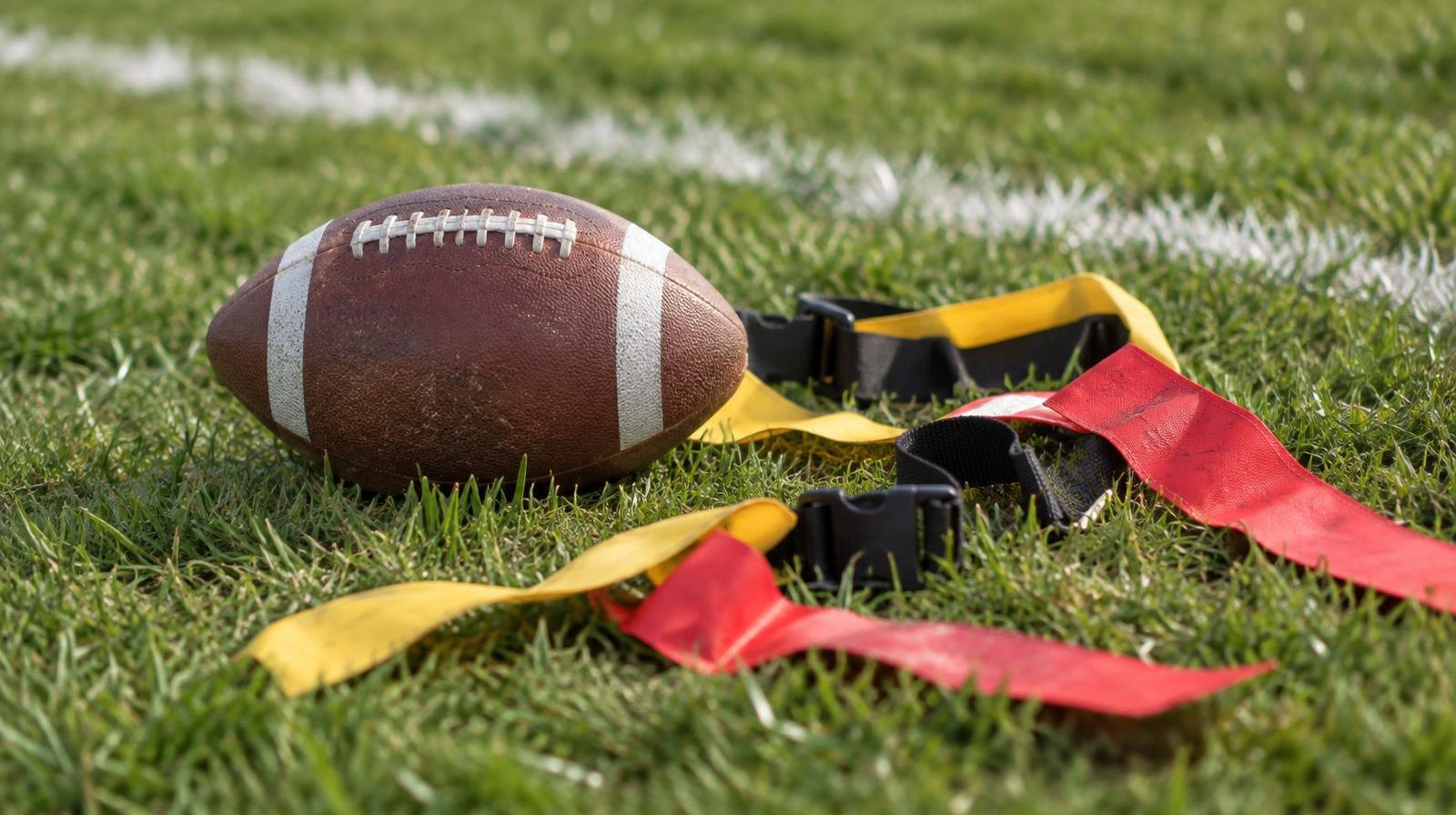 A football and flag football belts with flags laid on green grass.