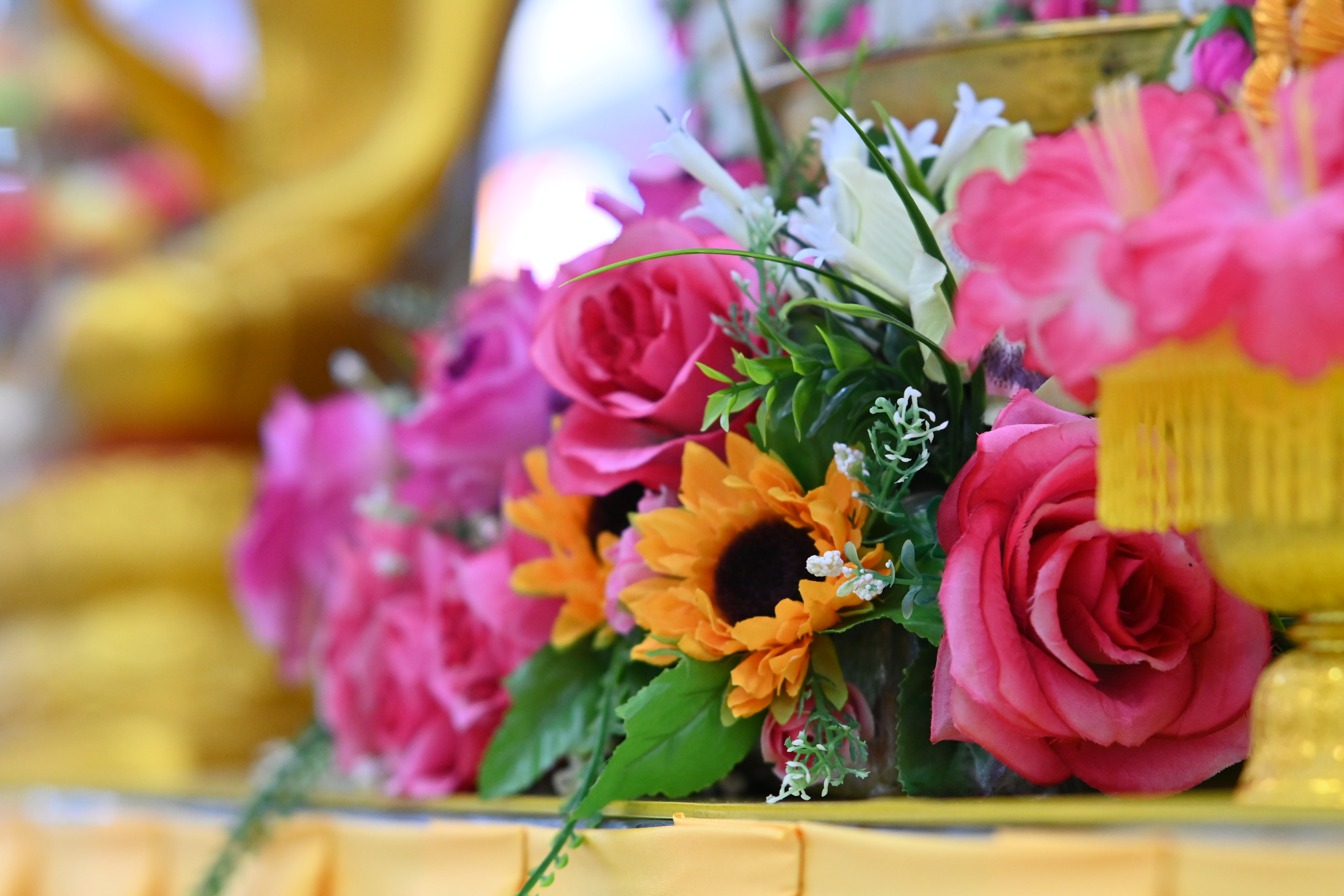 Vibrant bouquet of pink roses and an orange sunflower with green foliage.
