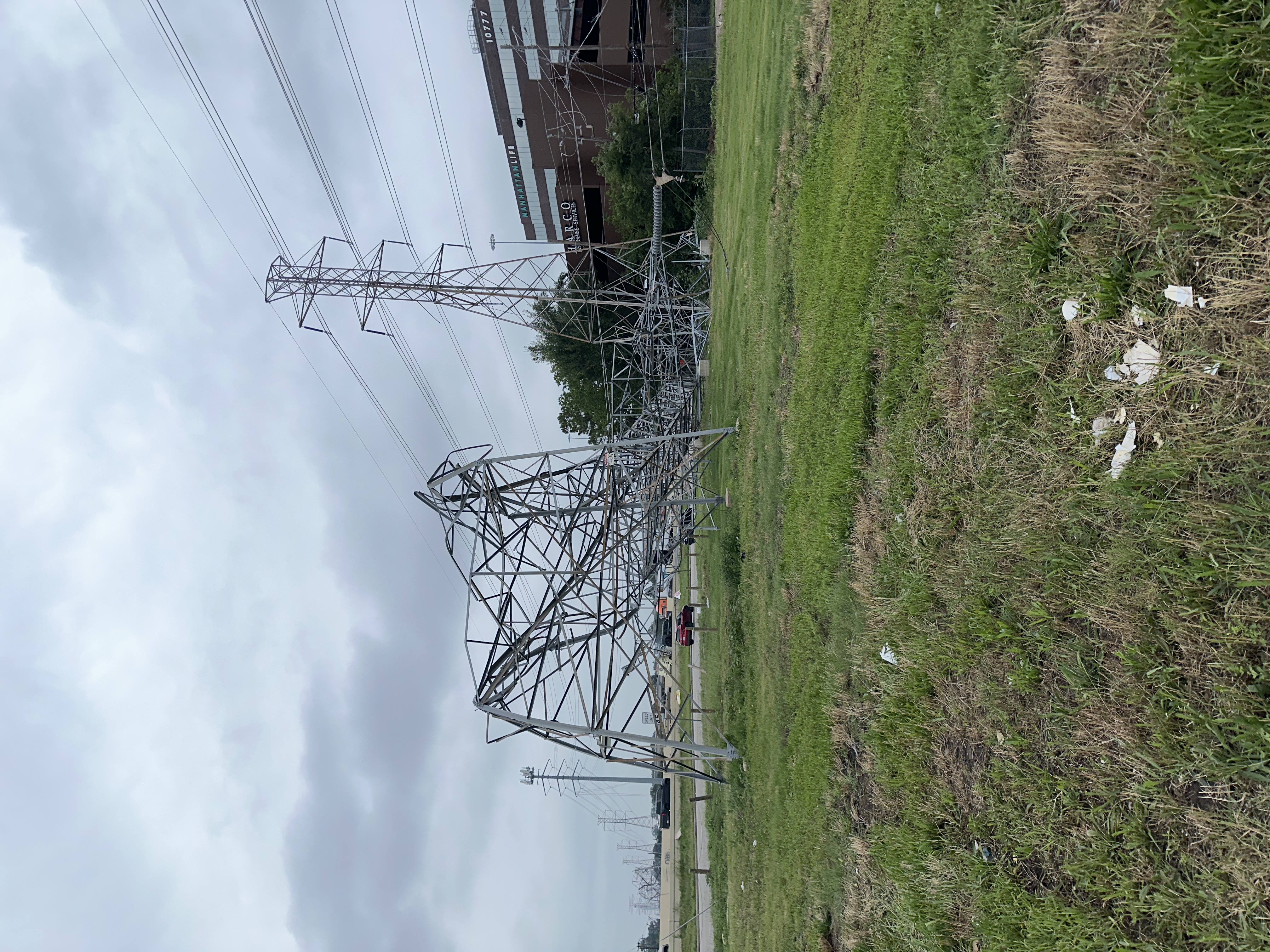 A collapsed steel lattice transmission tower leaning heavily to one side in a grassy field.