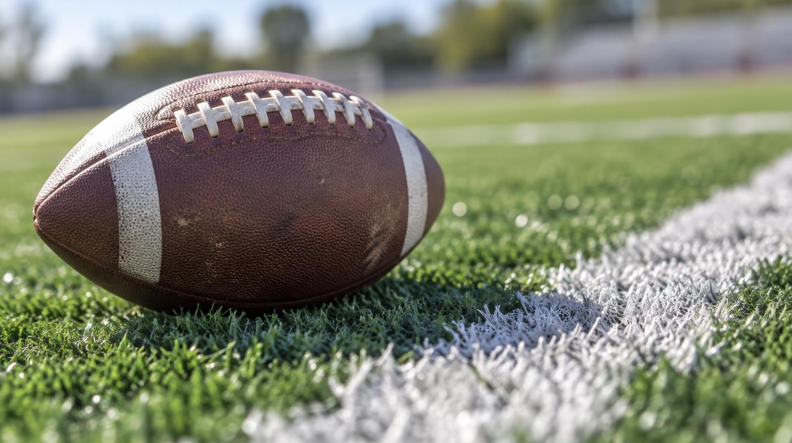 An American football resting on green artificial turf beside a white yard line.